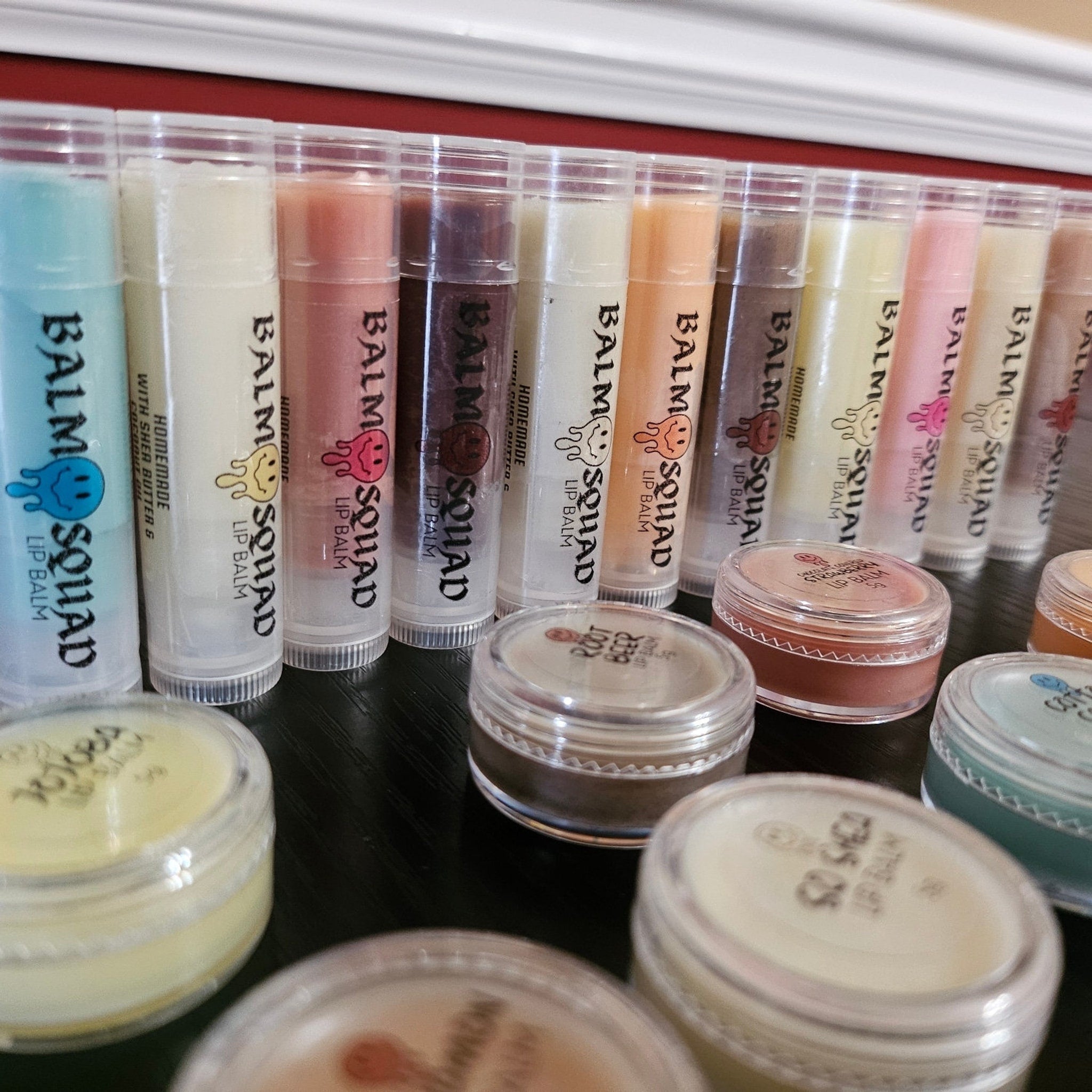 Lip balm tubes in various colors with "BALM SQUAD" text, clear plastic tubes, and small jars