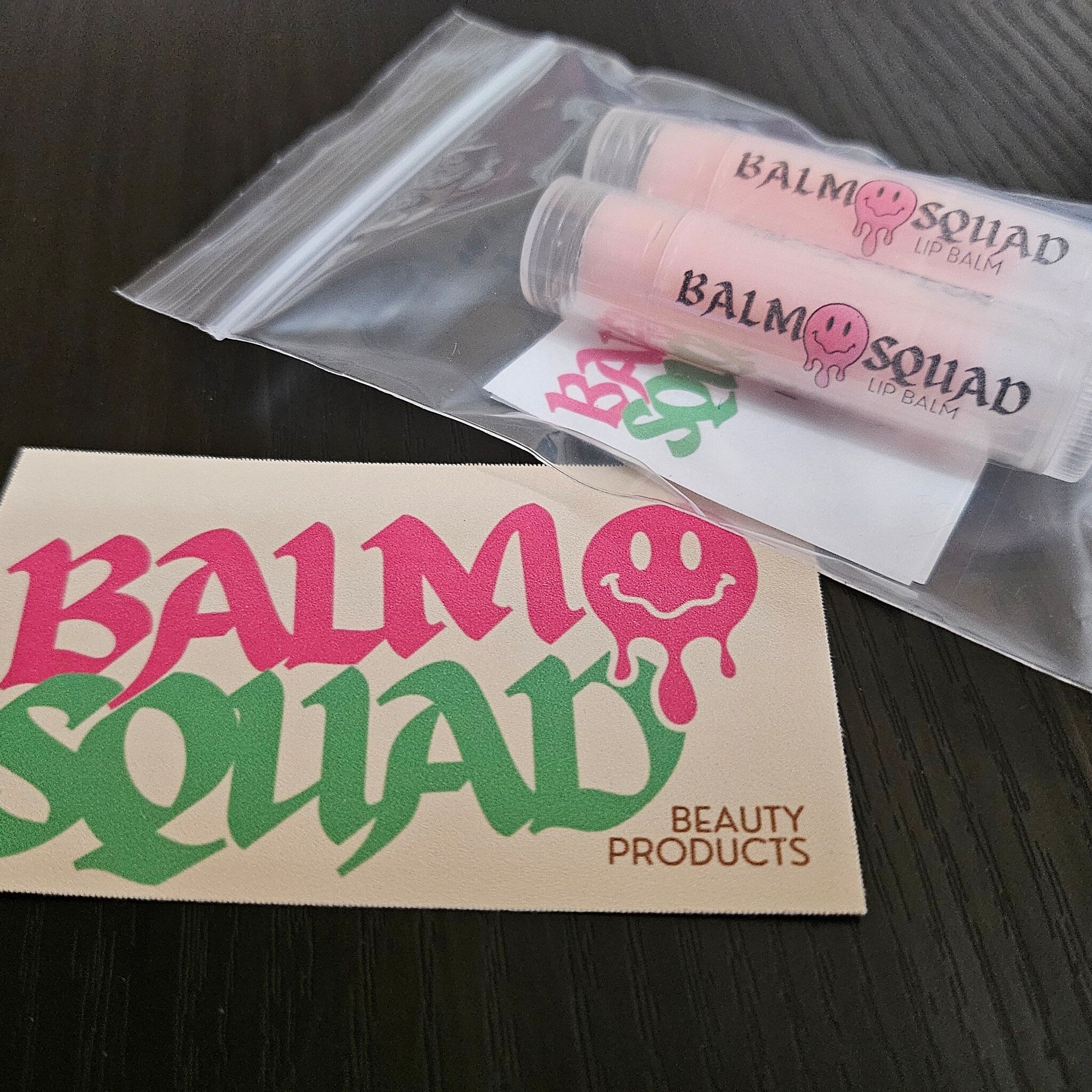 Lip balm tubes with pink color, clear plastic packaging, and Balm Squad text on white label