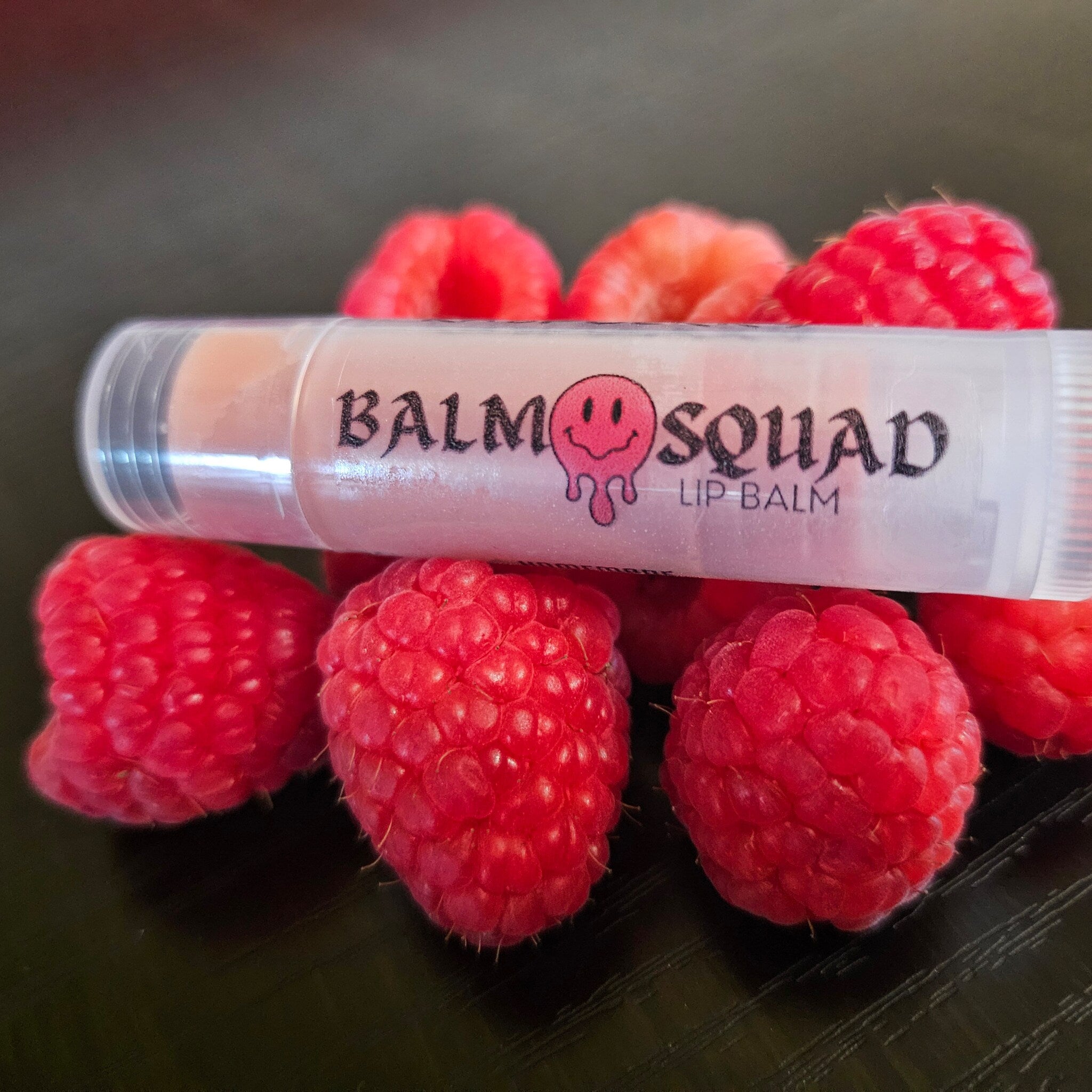 Lip balm tube with "BALM SQUAD" text, clear plastic, and raspberries with red color