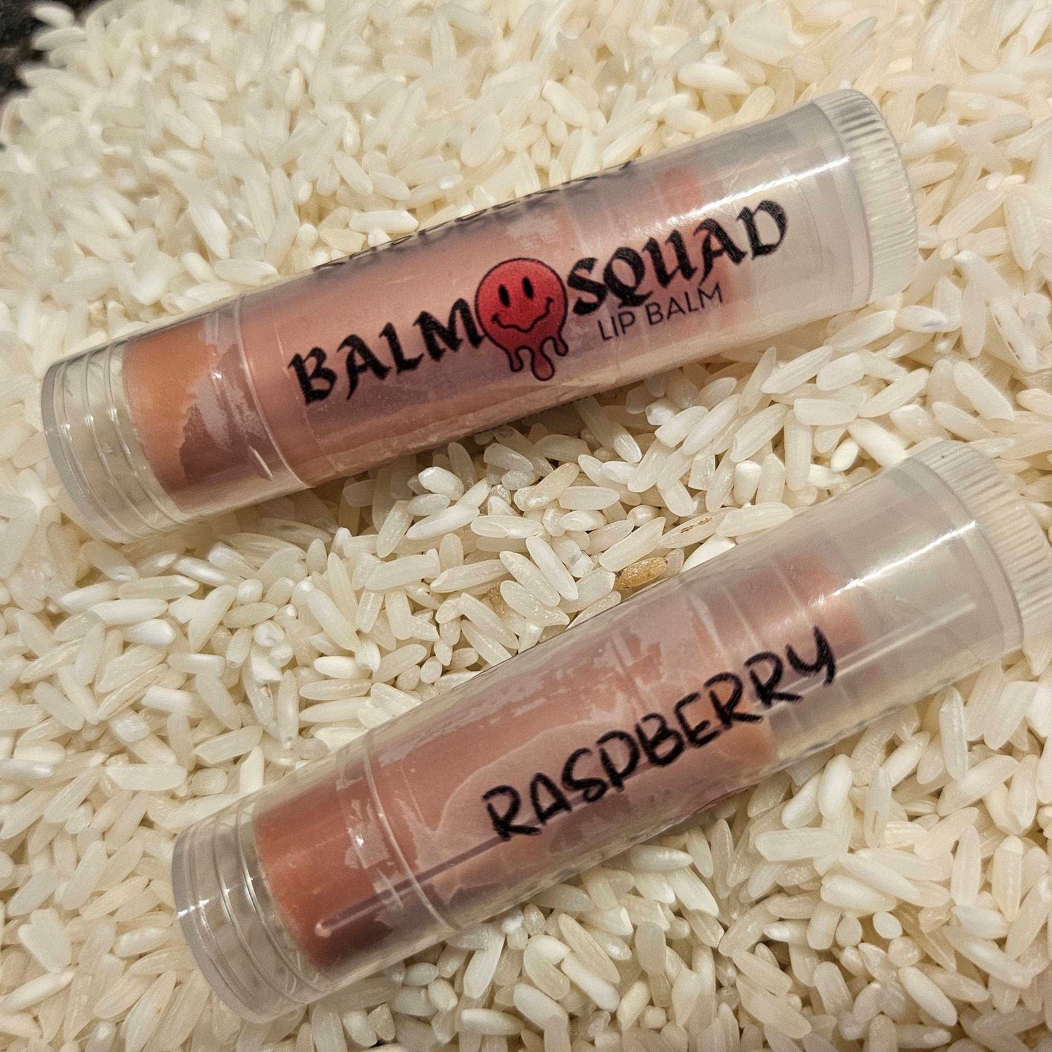 Lip balm tubes with pink tint and clear plastic, "Balm Squad" and "Raspberry" text visible