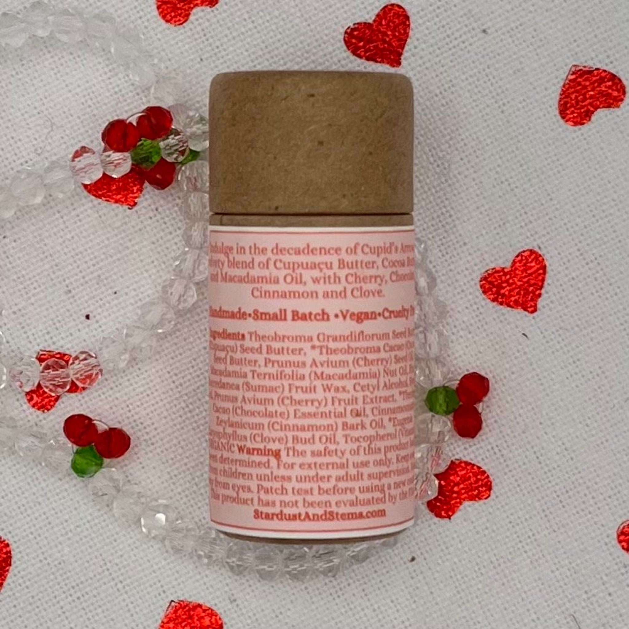 Lip balm tube with brown cap, pink label, and red accents on white fabric