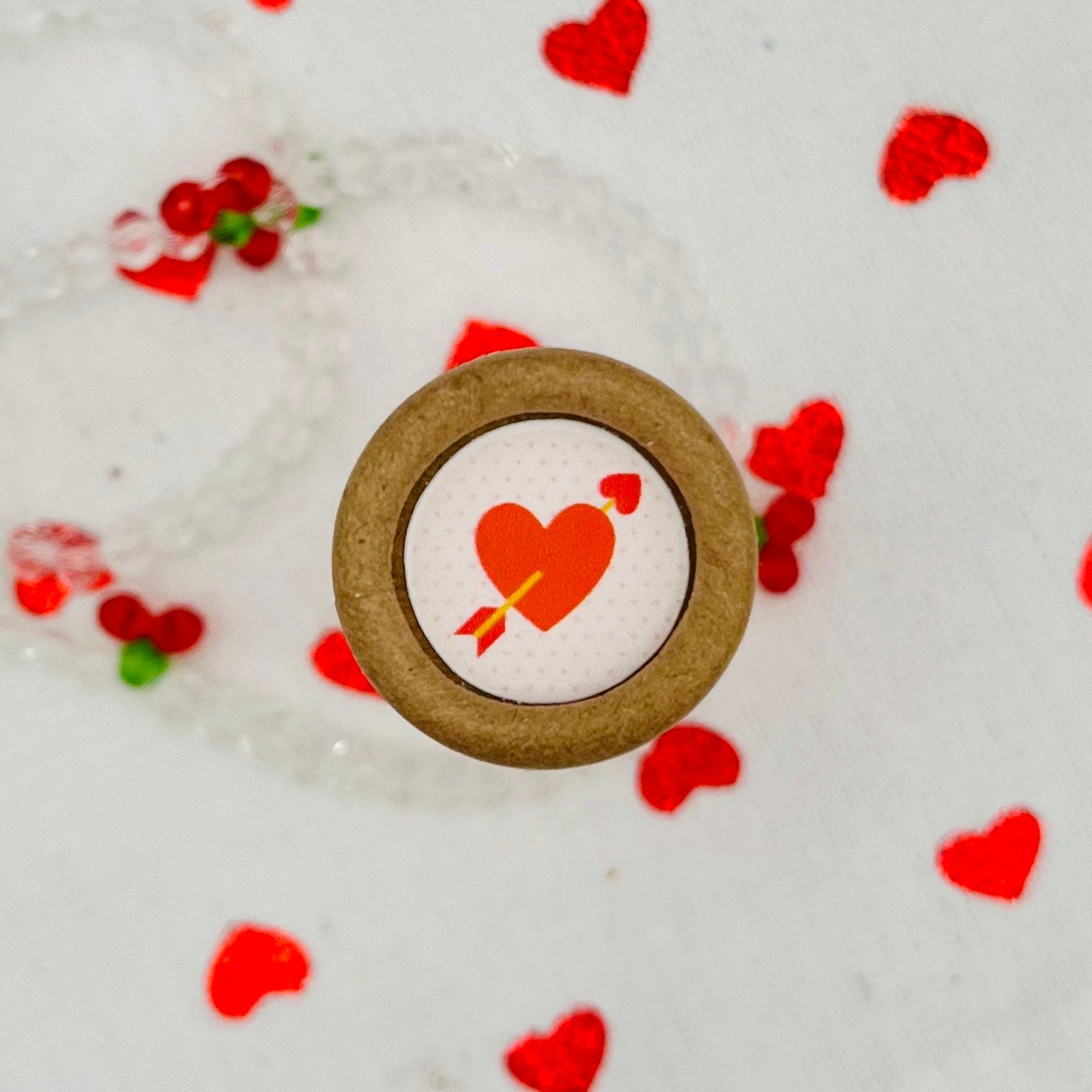 Heart shaped button with red heart and arrow, brown border, white background with red hearts
