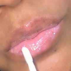 Lip gloss with pink shimmer, glossy finish, and applicator wand in use