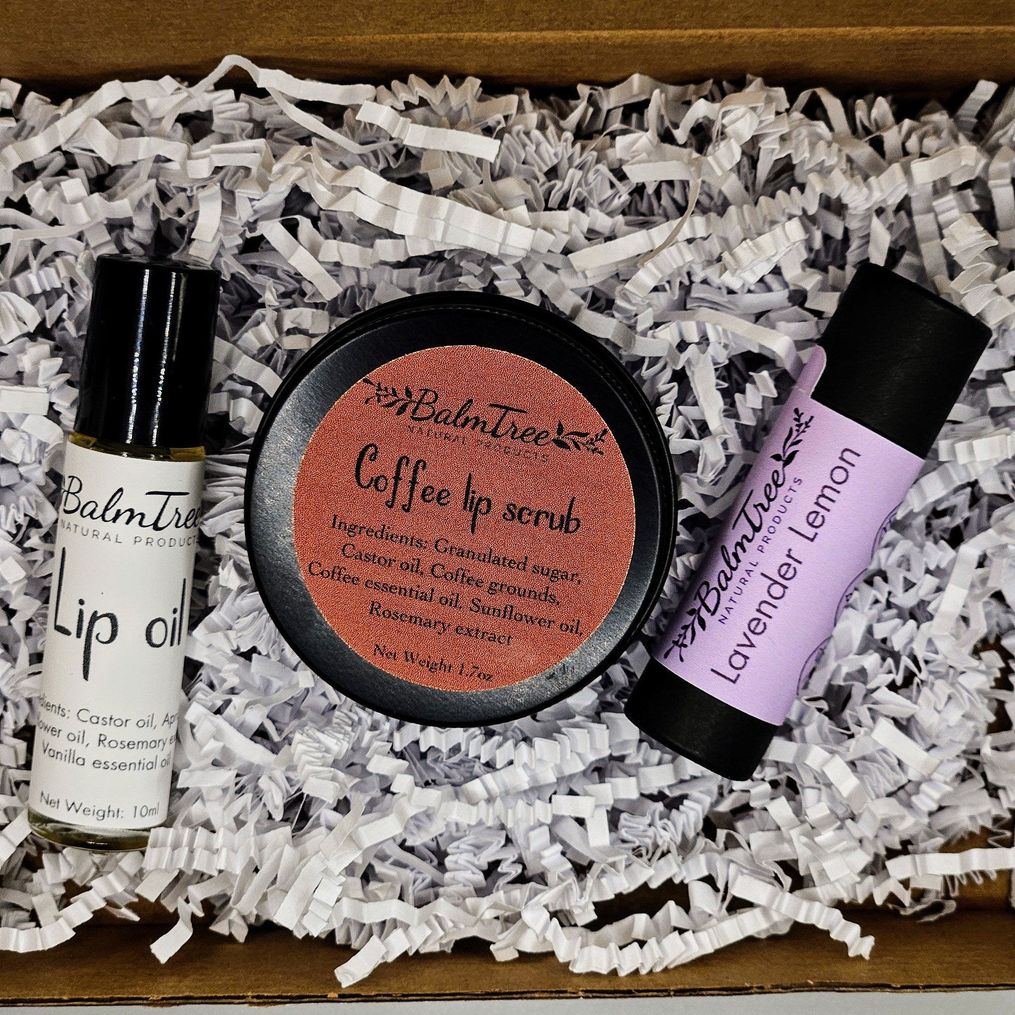 Lip care products in a box with white paper filler, BalmTree lip oil, scrub, and balm