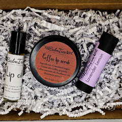Lip care products in a box with white paper filler, BalmTree lip oil, scrub, and balm