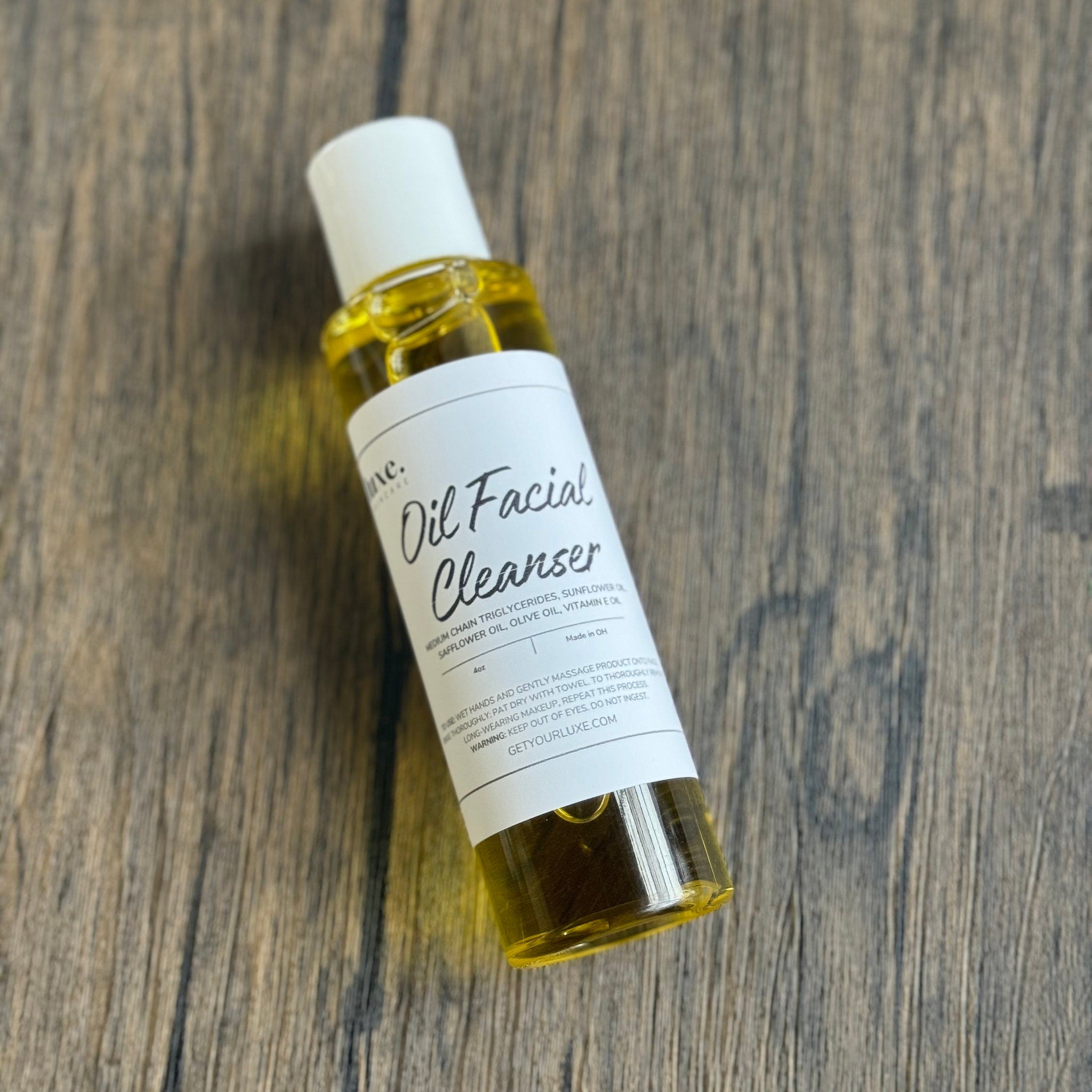 Oil facial cleanser bottle with white label, clear liquid, and white cap on wooden surface