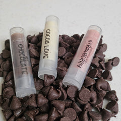 Lip balms with clear tubes, pink, brown, and white balm, on chocolate chips