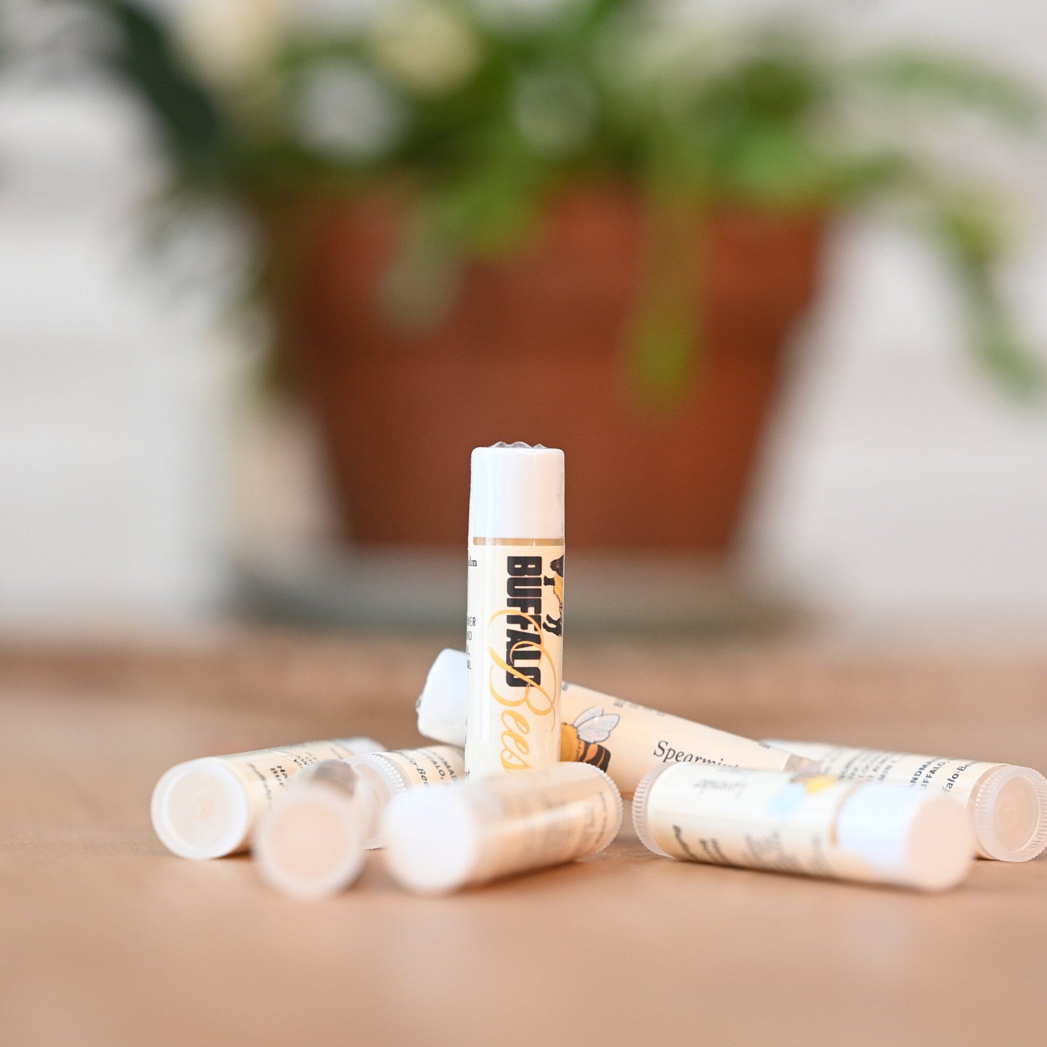 Lip balm tubes with white and tan labels, Buffalo Bees text, lying on a brown surface