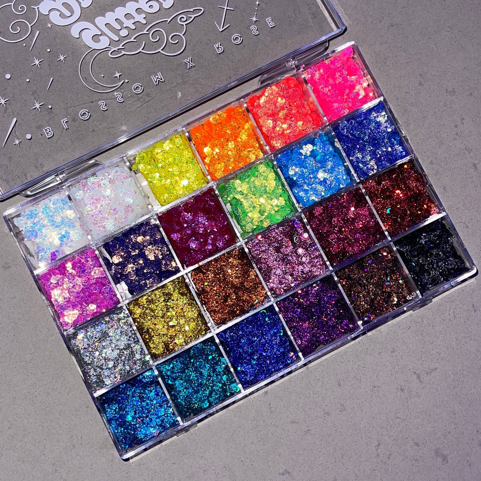 Close-up of 24 glitter gel eyeshadow shades in a palette with bold black sparkles and creamy textures