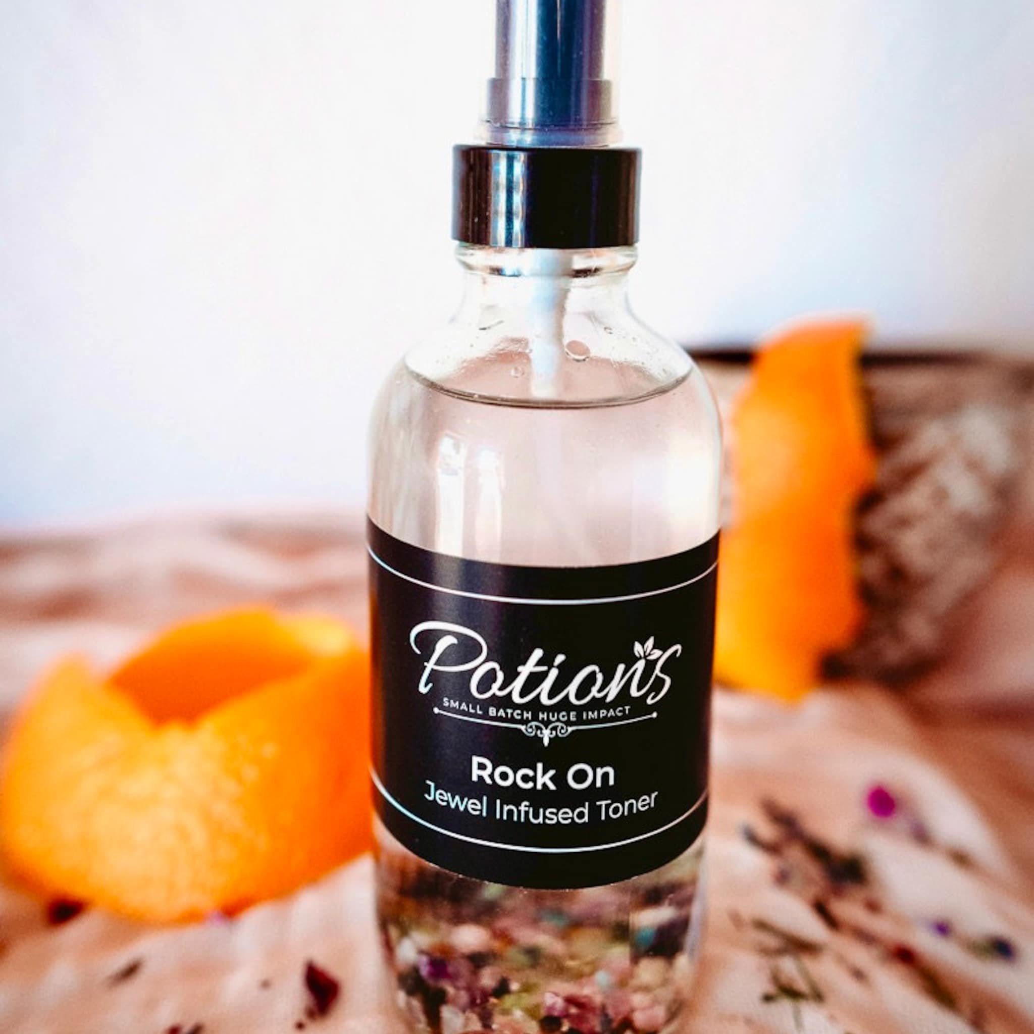 Facial toner bottle, clear glass, black label with "Potions" text, citrus fruit visible