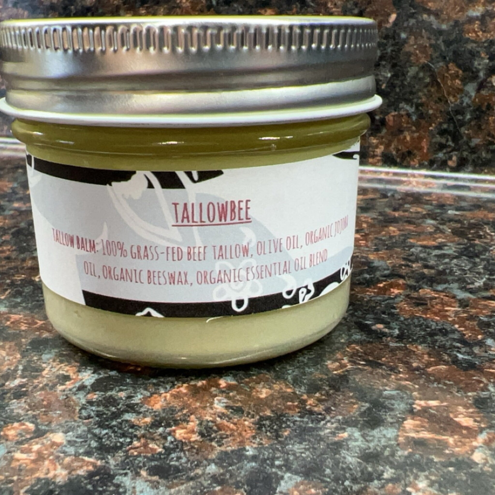 Tallow balm jar with silver lid, white label, and green contents, TALLOWBEE brand