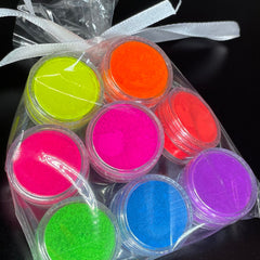 Side view of eight vibrant neon matte eyeshadow pans in fluorescent pink, orange, yellow, green, blue, purple, white, and black