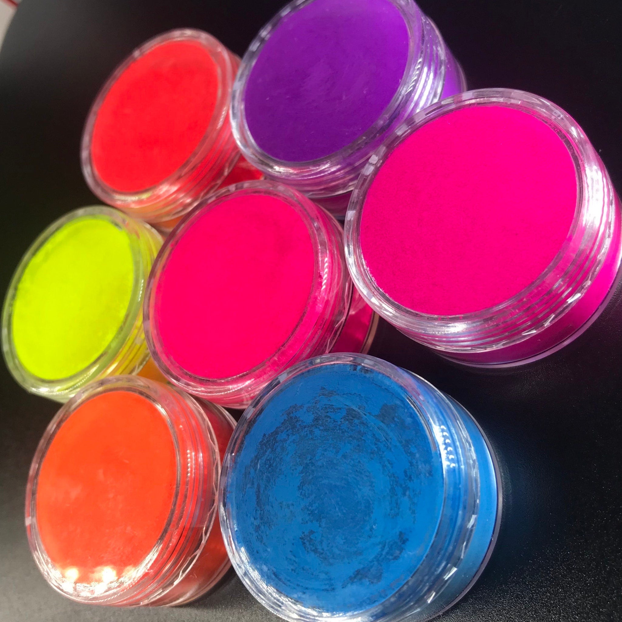 Eight vibrant neon matte eyeshadow pans with UV glow pigments in a sleek black palette