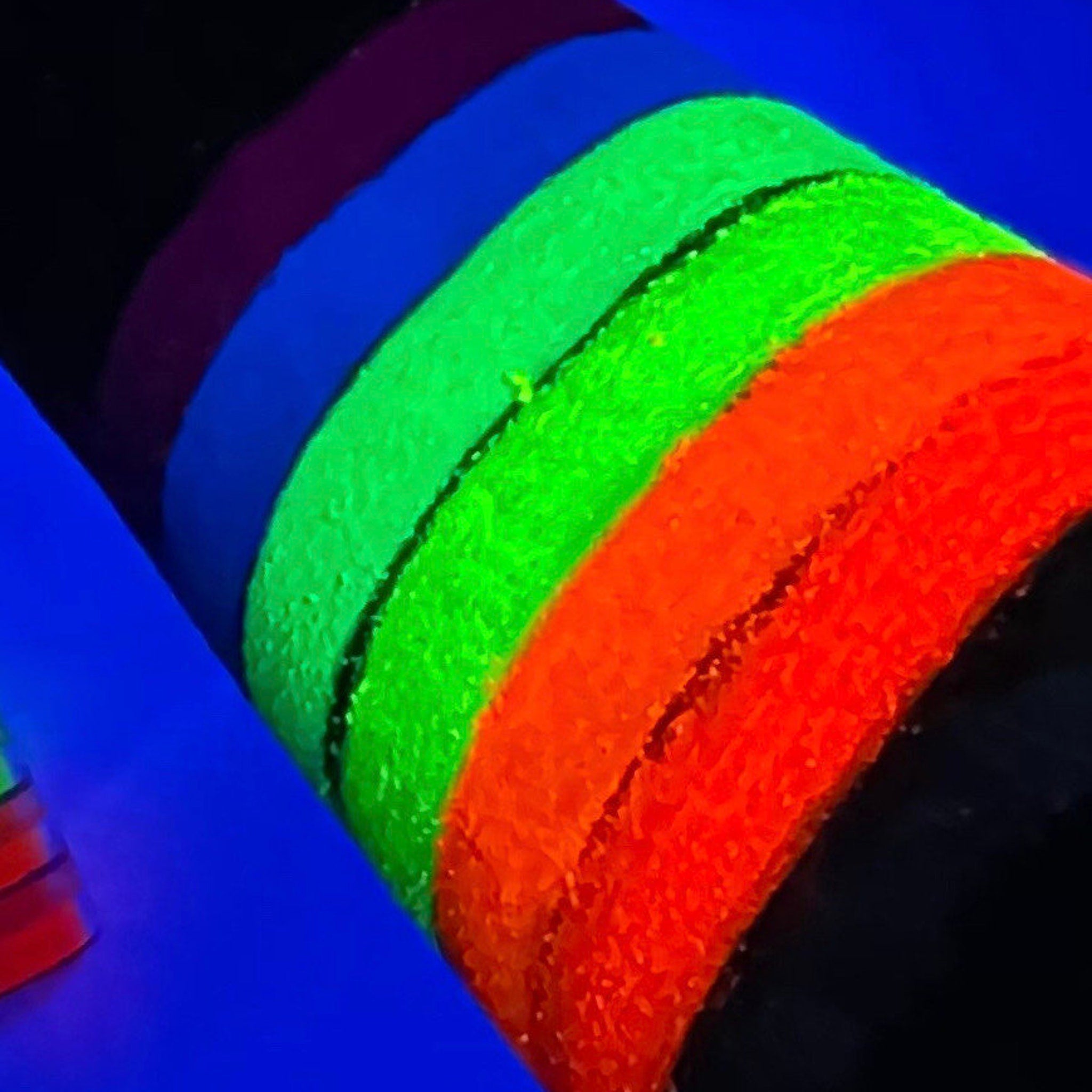 Seven vibrant neon matte eyeshadows in round pans arranged in a rainbow gradient on white background