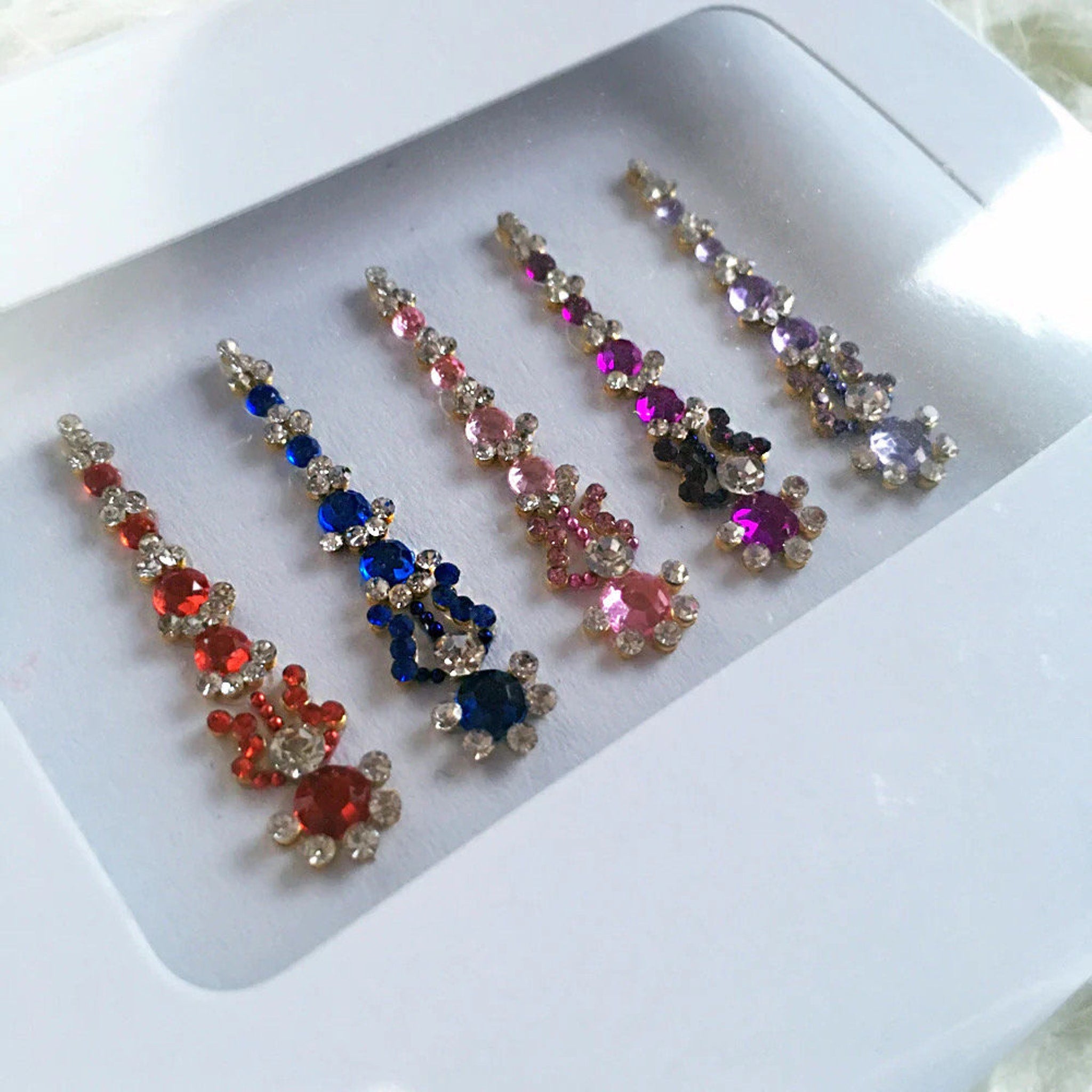 Jeweled accessories with red, blue, pink, purple and gold accents, in a white box, for decorative use