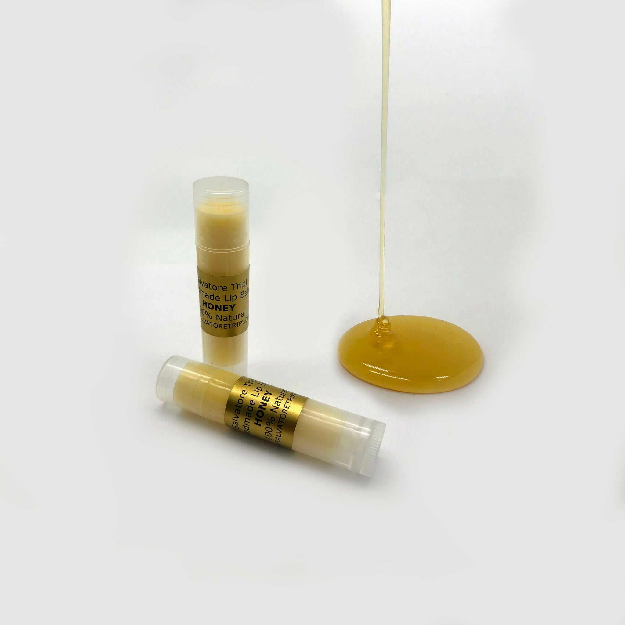Lip balm tubes with yellow balm, clear plastic, and honey drip on white surface