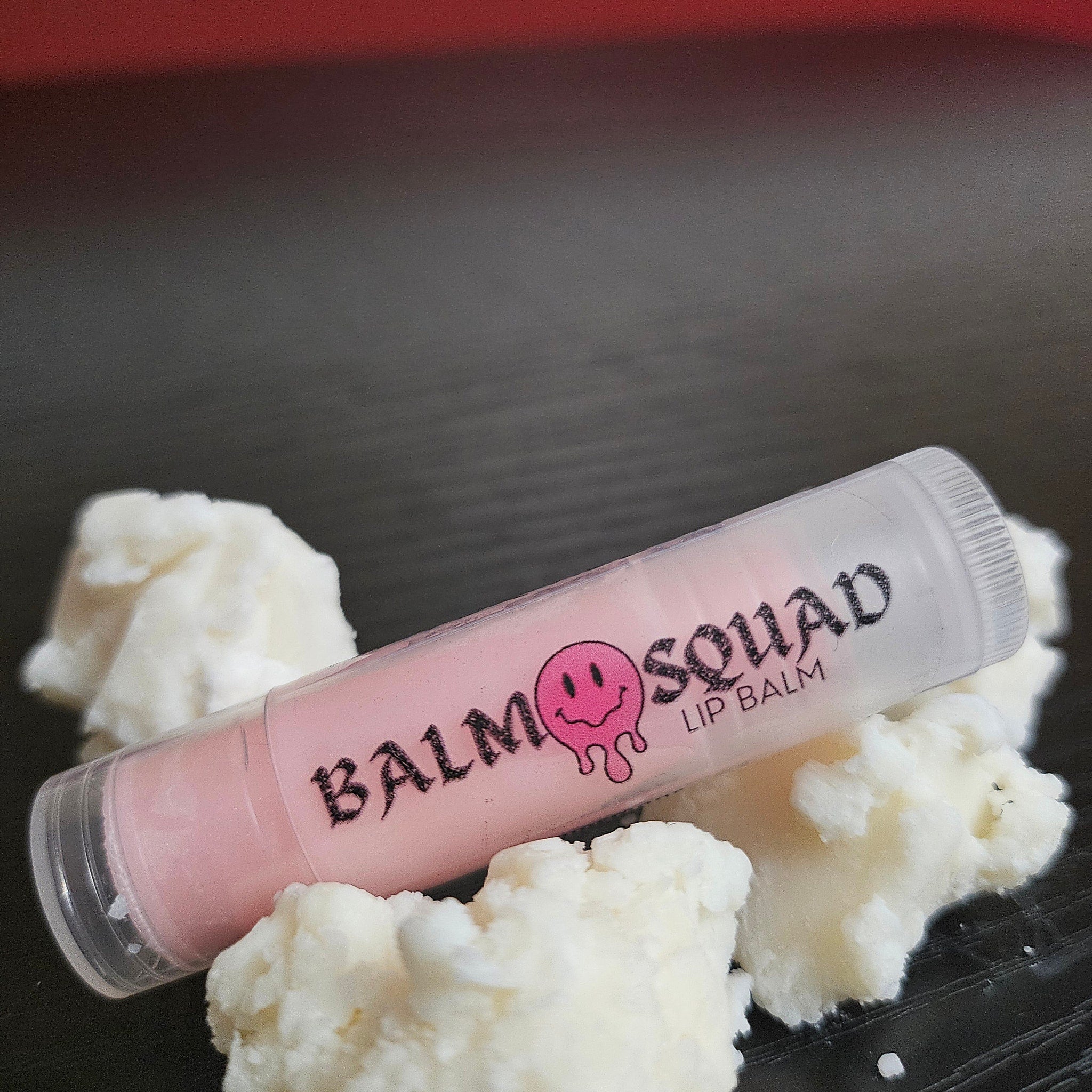 Lip balm in clear tube with pink balm, white text, and white substance around it
