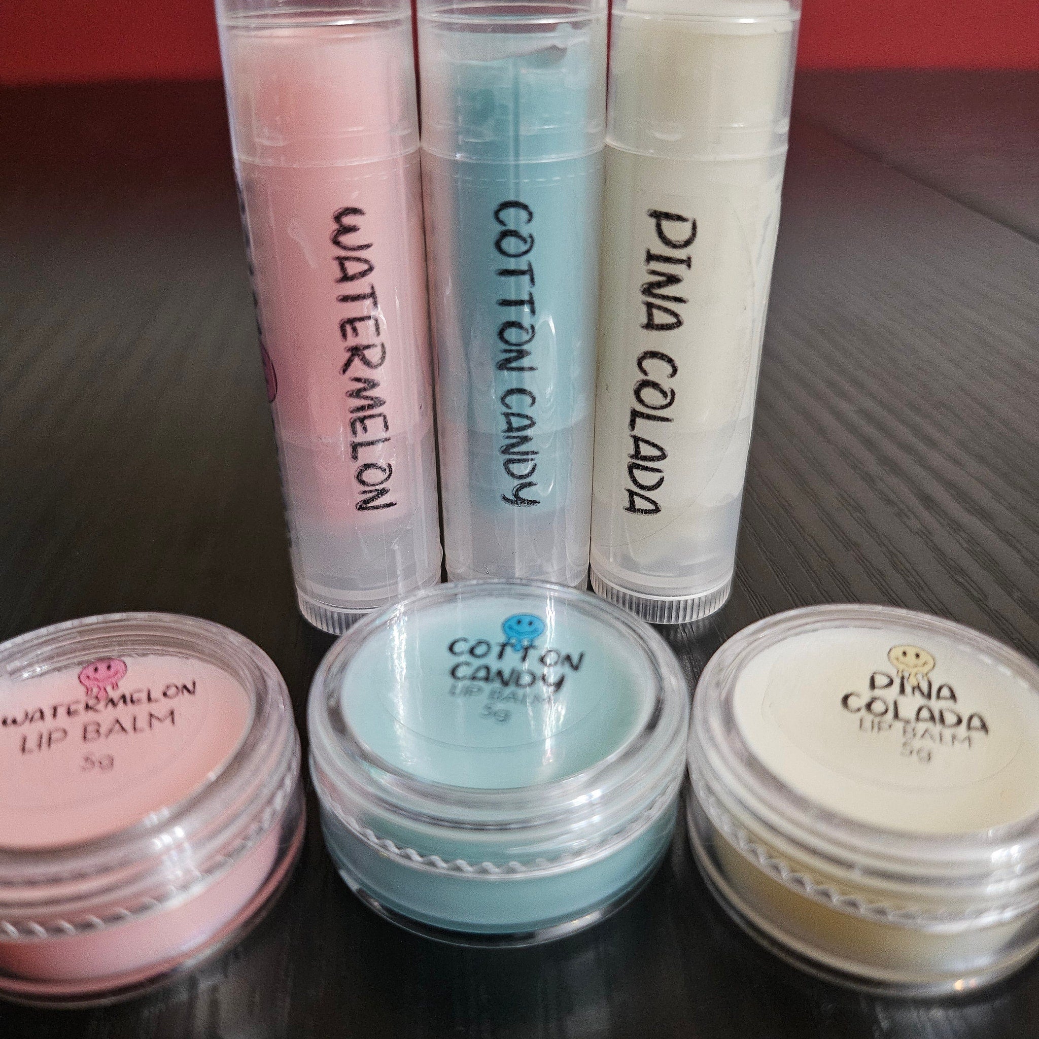 Lip balm tubes in pink, blue, and white with handwritten labels and matching lip balm pots