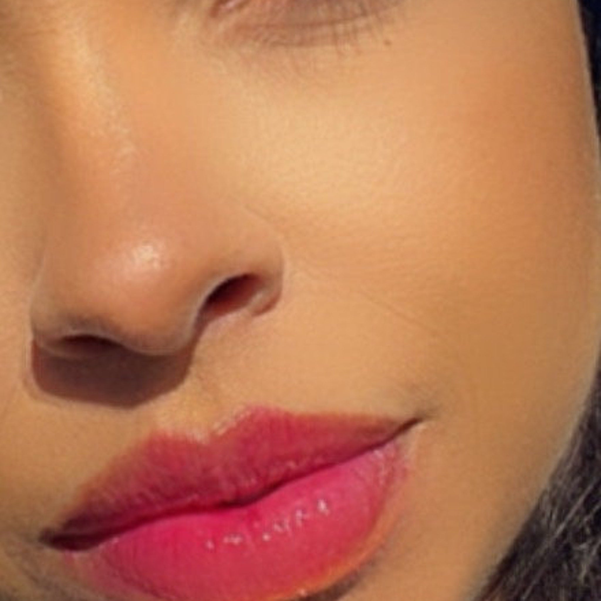 Lip gloss with pink color, glossy finish, and visible skin texture on face