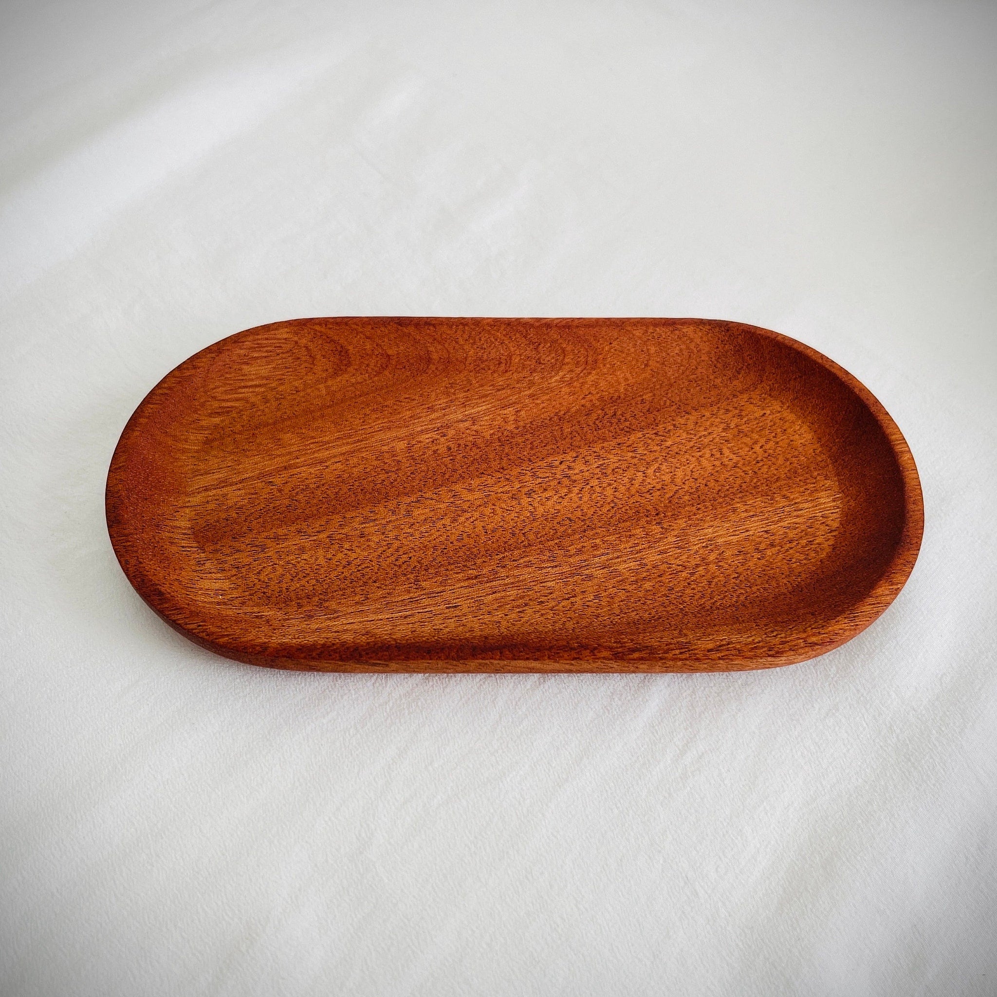 Wooden serving tray, oval shape, brown wood grain, on white fabric surface