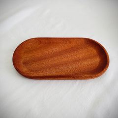 Wooden serving tray, oval shape, brown wood grain, on white fabric surface