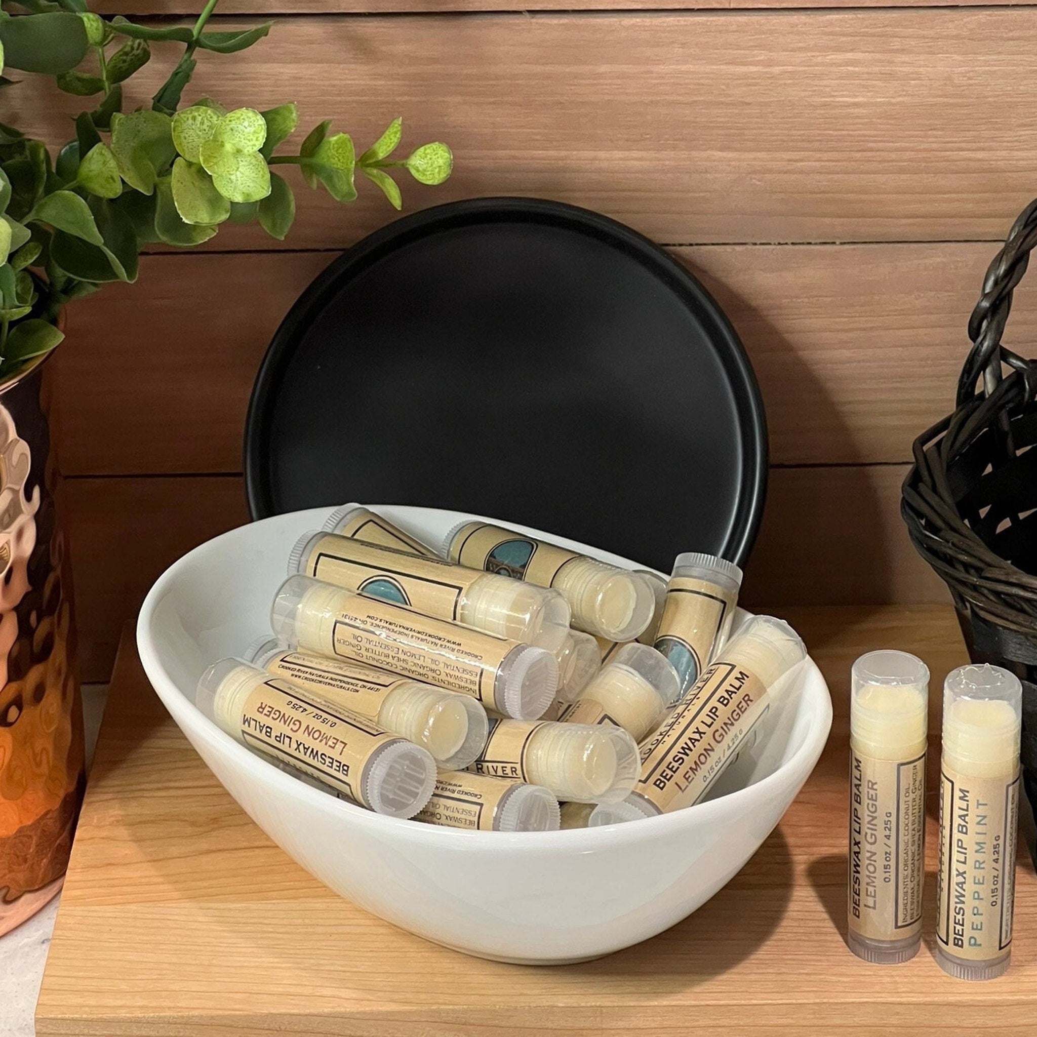 Beeswax lip balm tubes in white bowl with Crooked River Naturals label, wood background