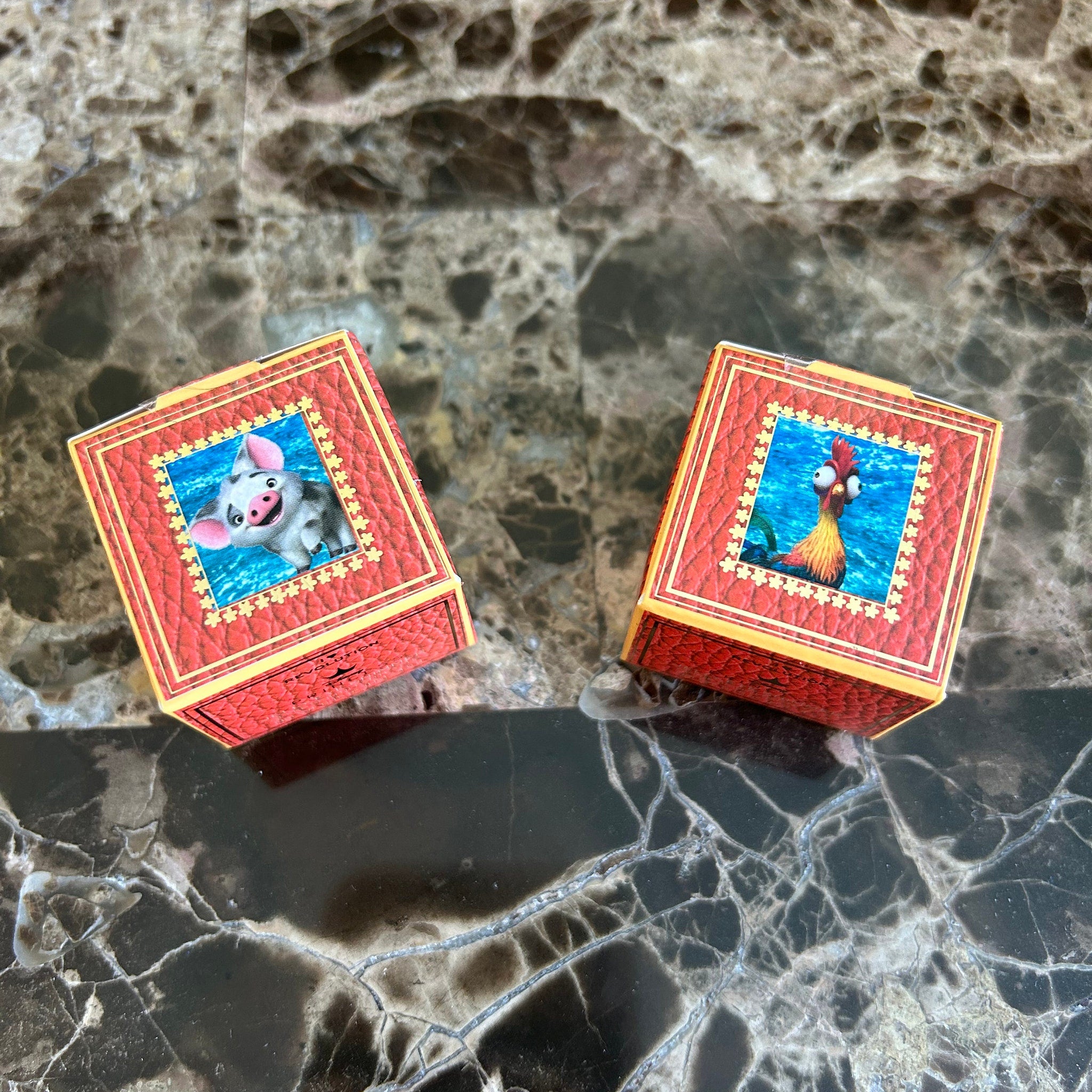Eye shadow boxes with red leather-look texture and Disney character images on marble surface
