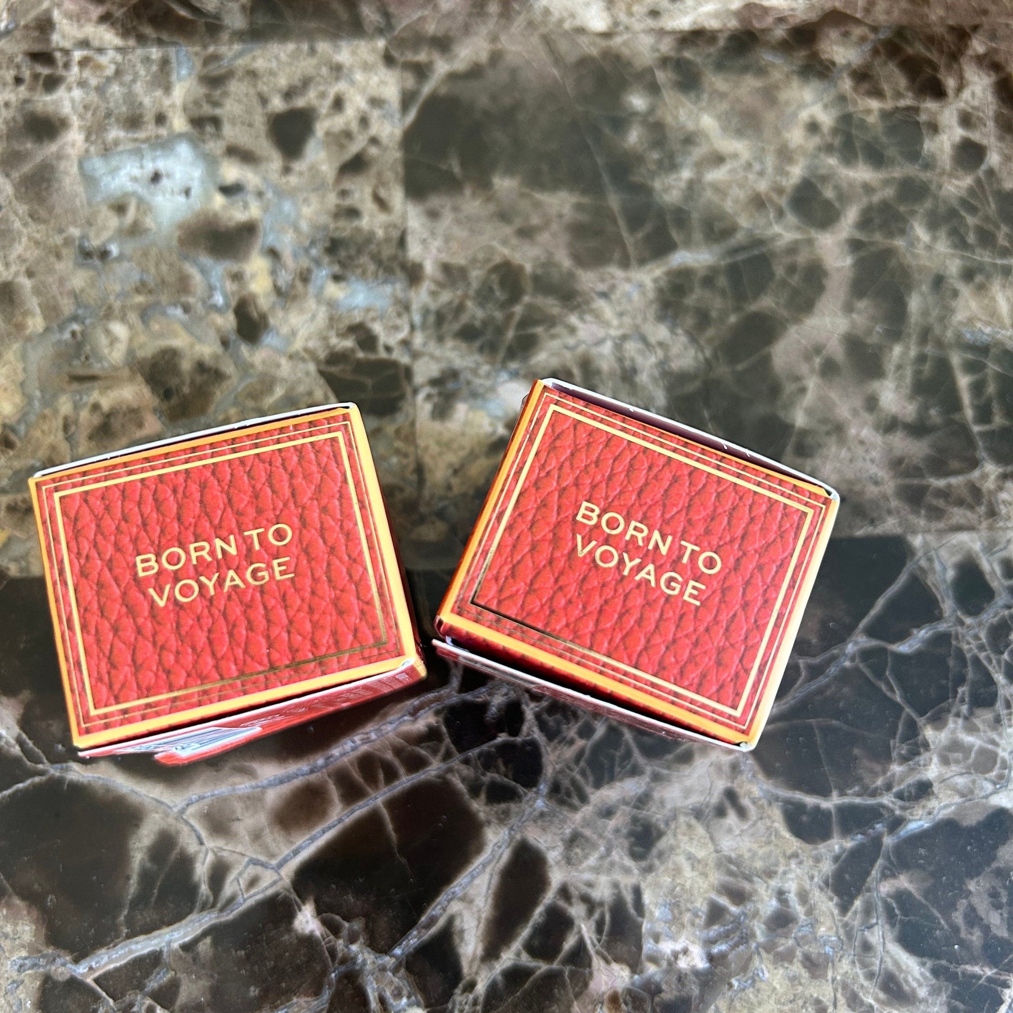 Red textured box with gold trim and "Born to Voyage" text on a marble surface