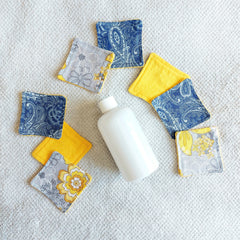 Makeup remover pads with floral fabric, yellow, blue, and gray patterns, on white towel with bottle