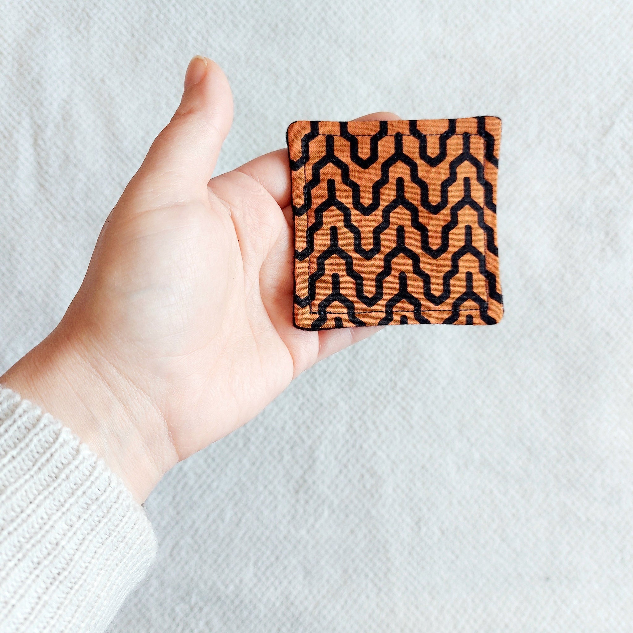Square patterned fabric in orange and black held in hand, geometric design, textile material