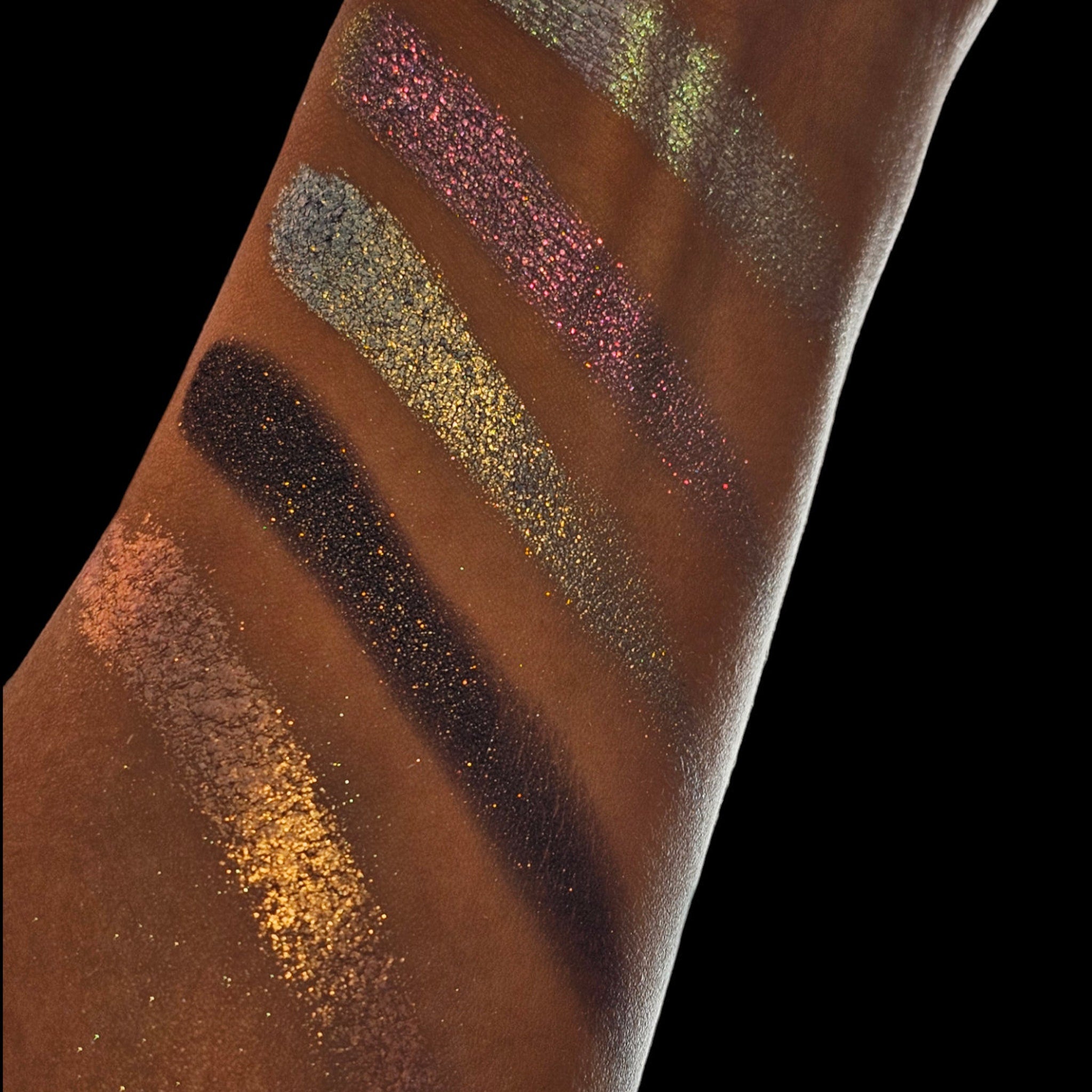 Side view of five multichrome pressed eyeshadow pans showing shifting shimmery hues in compact palette