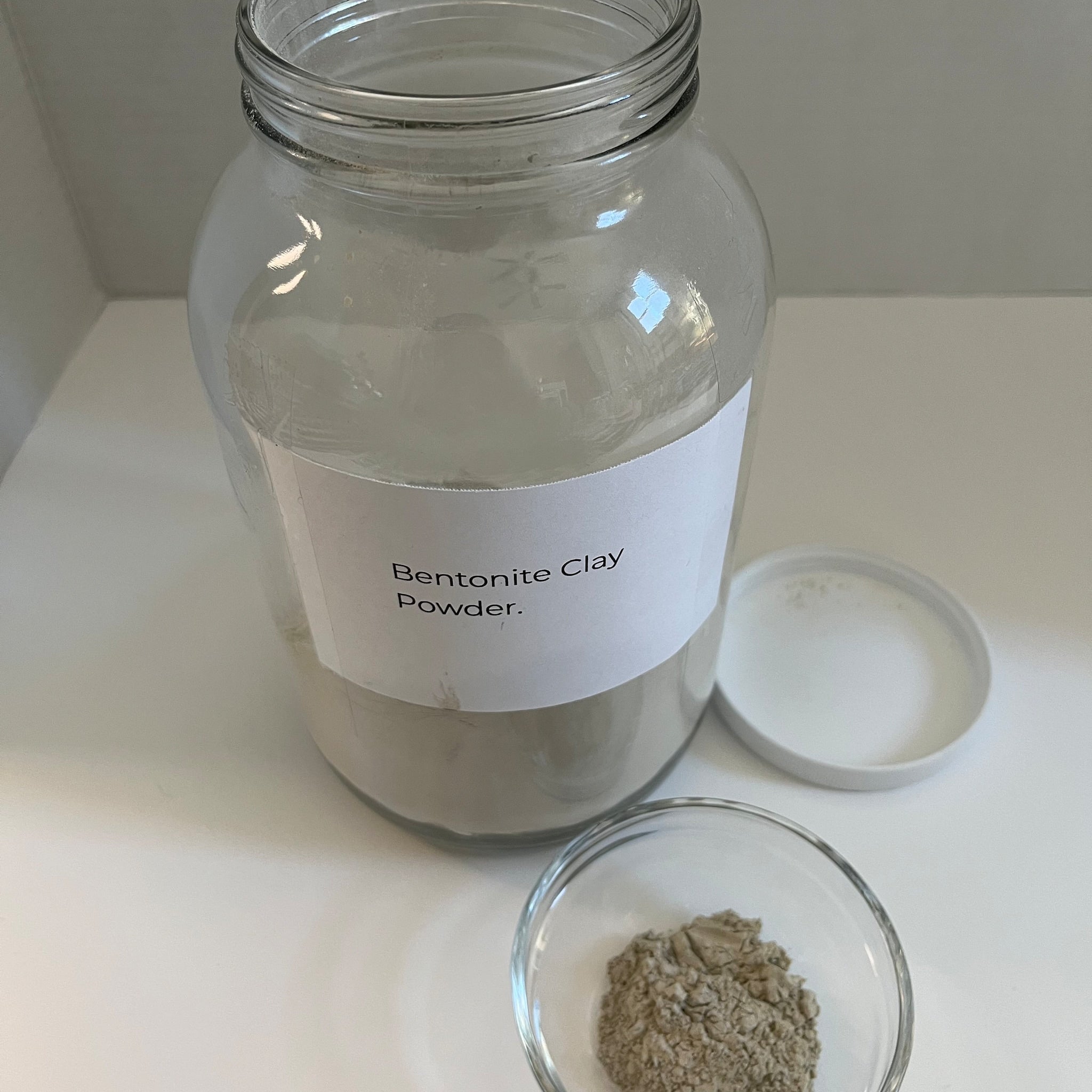 Bentonite clay powder in glass jar with white label, small bowl of clay and white lid