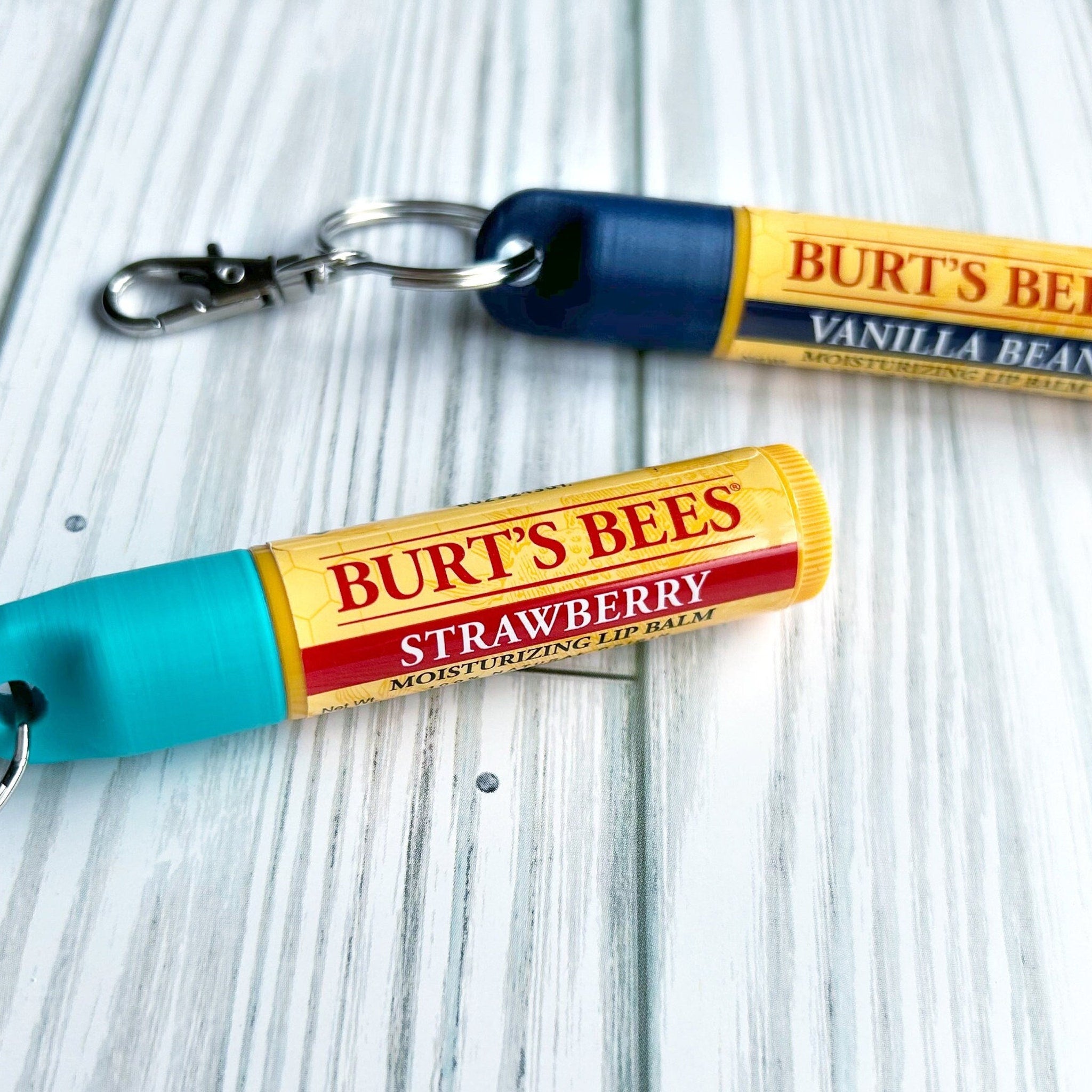 Lip balm tubes with Burt's Bees branding, yellow and red labels, blue and teal caps, on a light wood surface