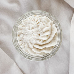 Whipped cream in a clear glass jar with a white, textured, swirled design, on a white cloth
