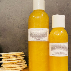 Side view of amber glass turmeric soap bottle with loofah, showcasing golden liquid cleanser texture and minimalist label design