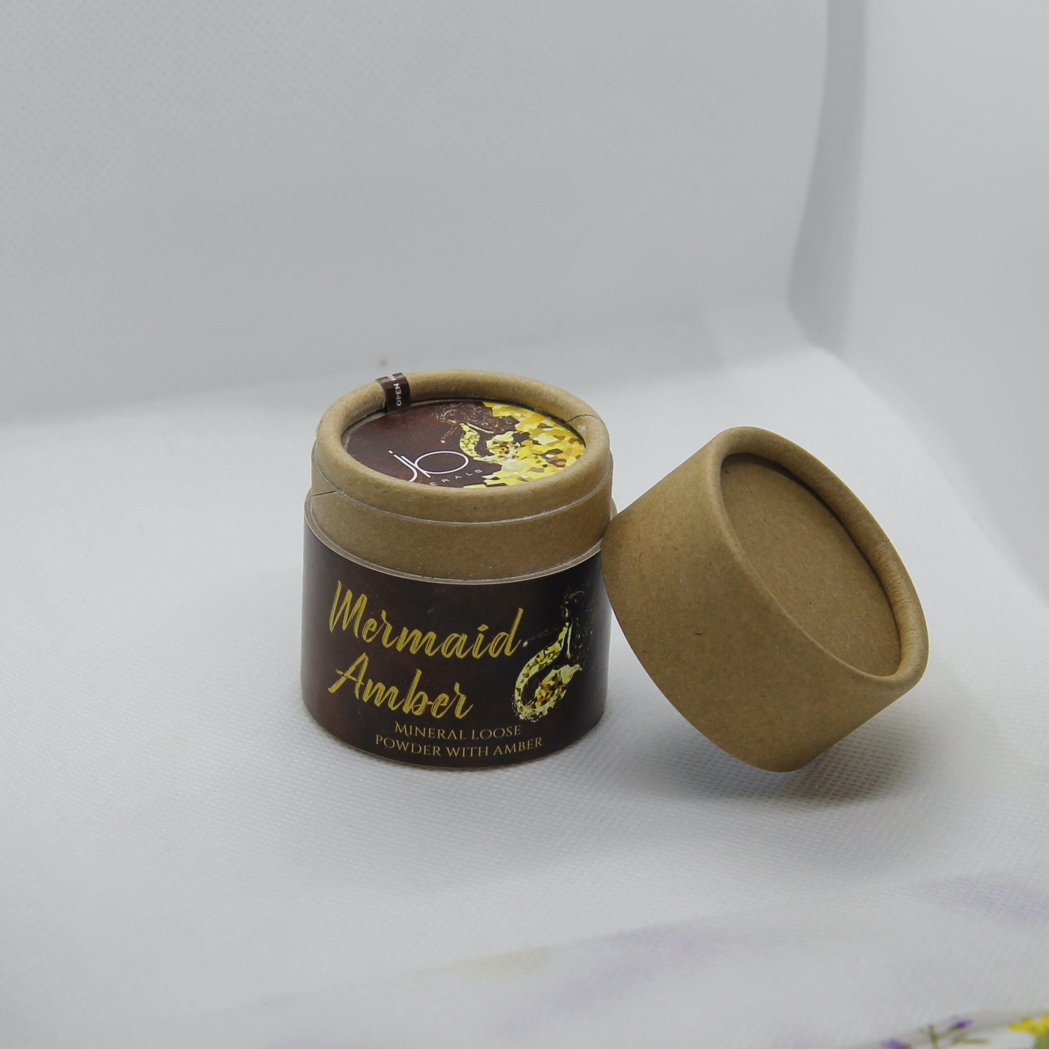 Mineral loose powder in brown and tan cardboard tube with Mermaid Amber text and lid off