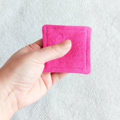 Pink felt square held in hand, showing stitched edges and textured material
