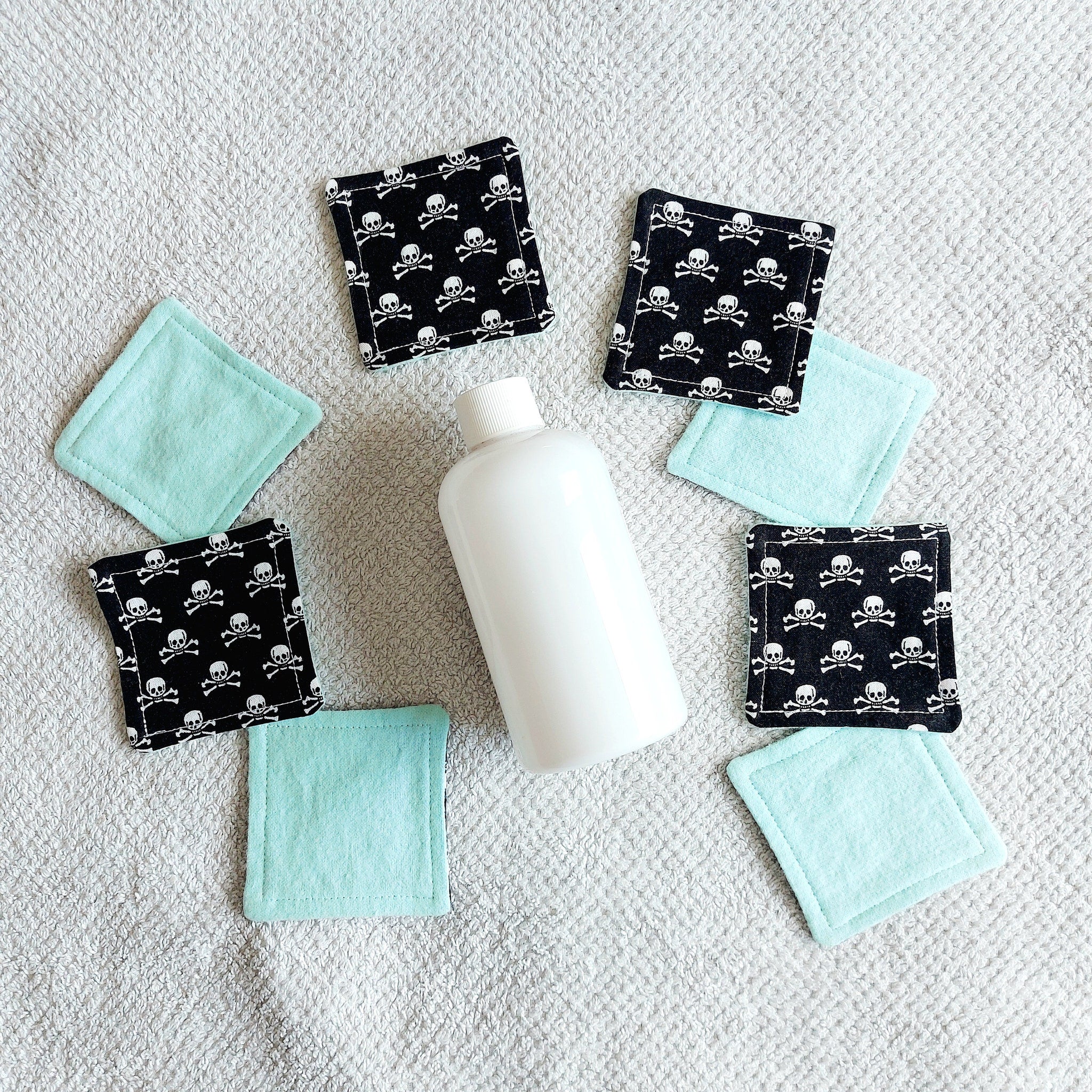 Makeup remover pads, black skull print fabric, and light blue fabric pads on a white towel
