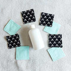 Makeup remover pads, black skull print fabric, and light blue fabric pads on a white towel