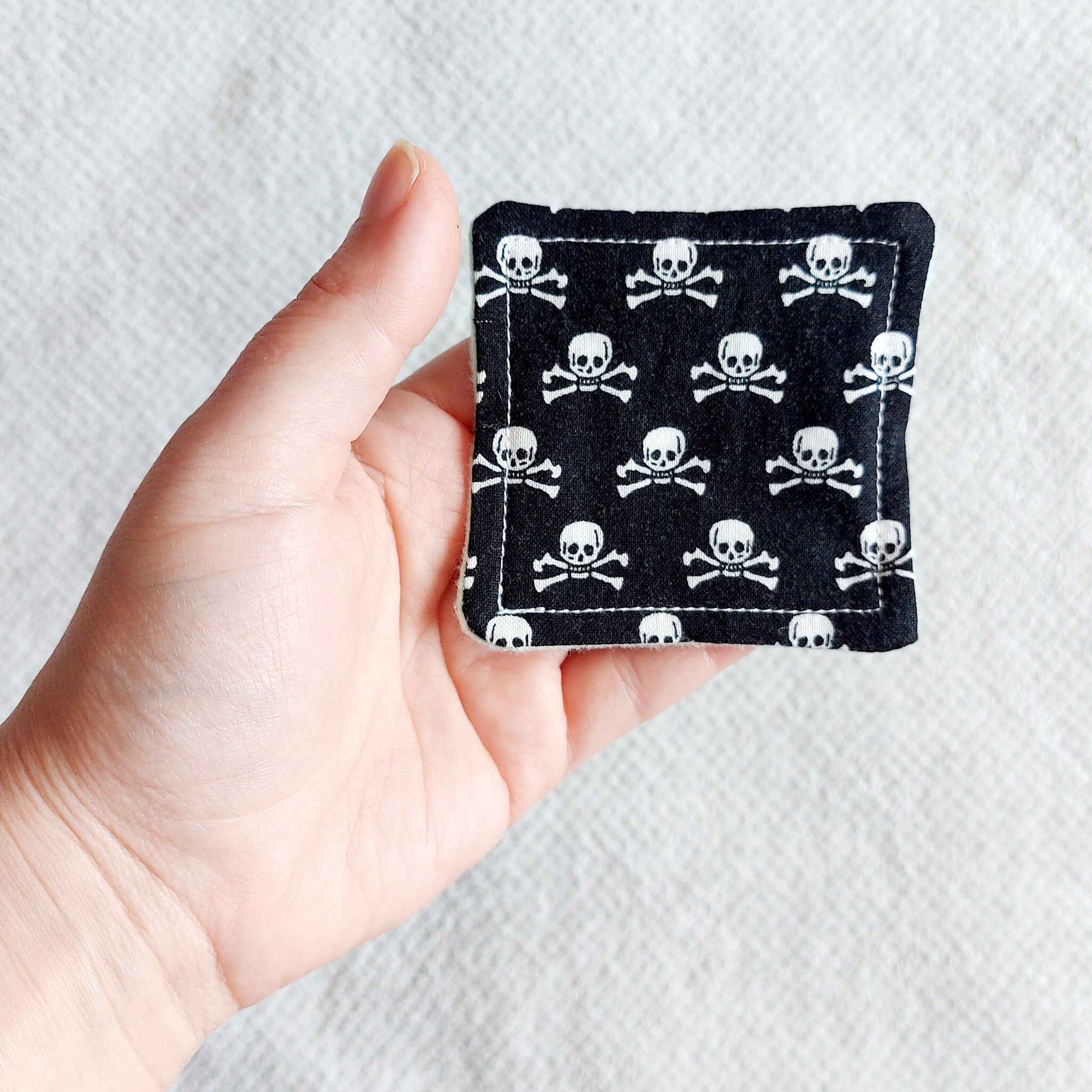 Square black fabric with white skull and crossbones pattern, held in hand