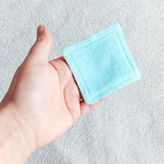 Reusable facial pad, square aqua blue fabric, held in hand