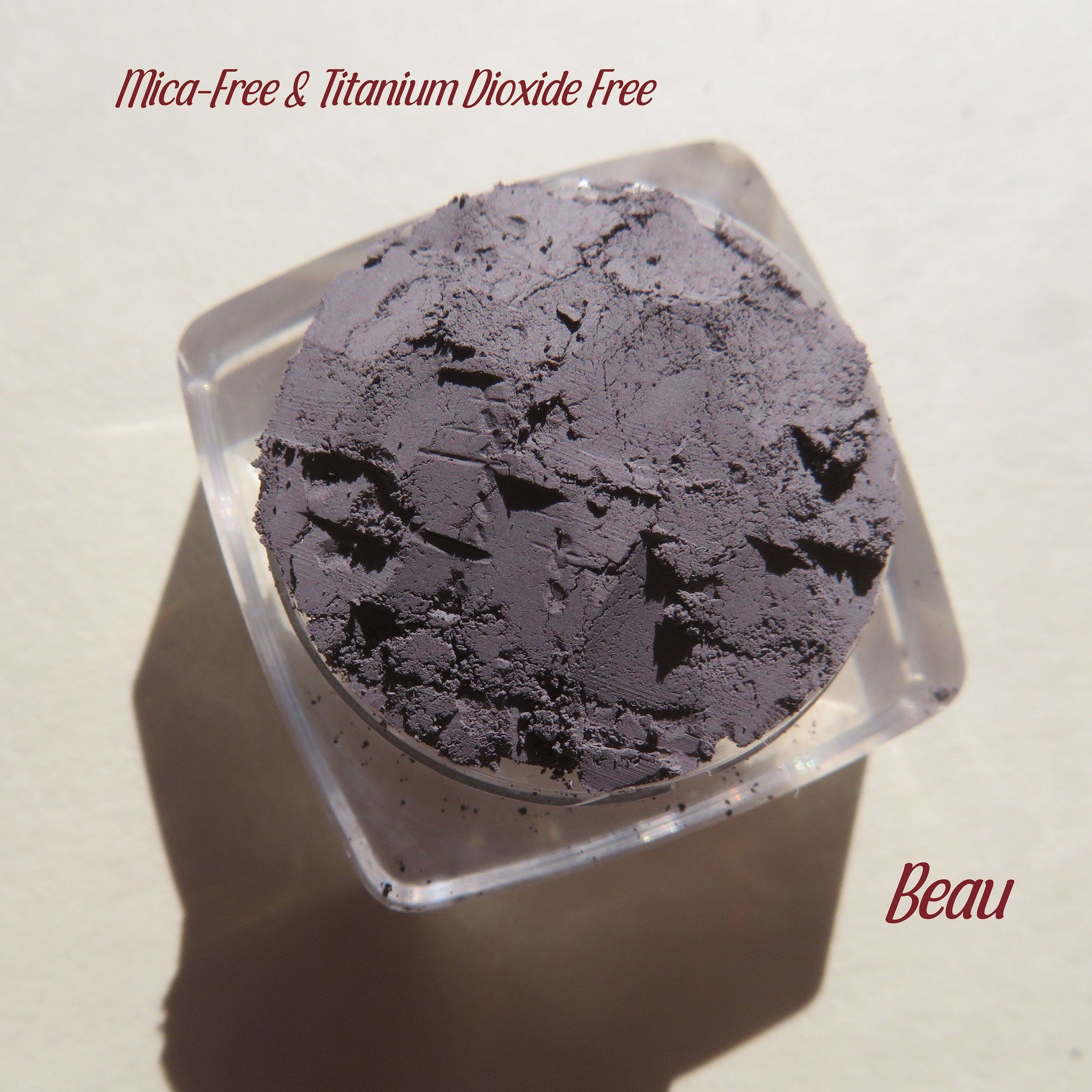 Powder eyeshadow in dark gray, textured, in a clear container, with "Beau" text visible.