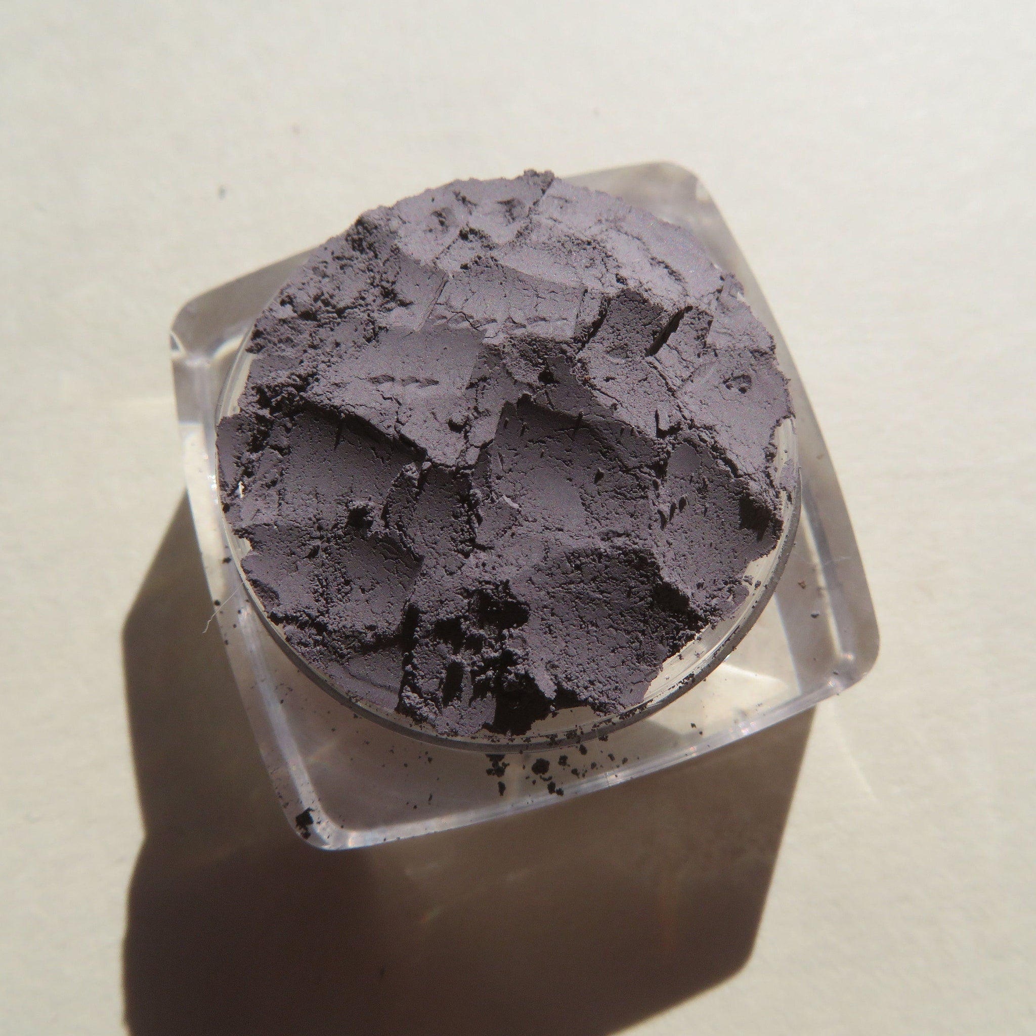 Powder eyeshadow in dark gray color, textured, in a clear plastic container