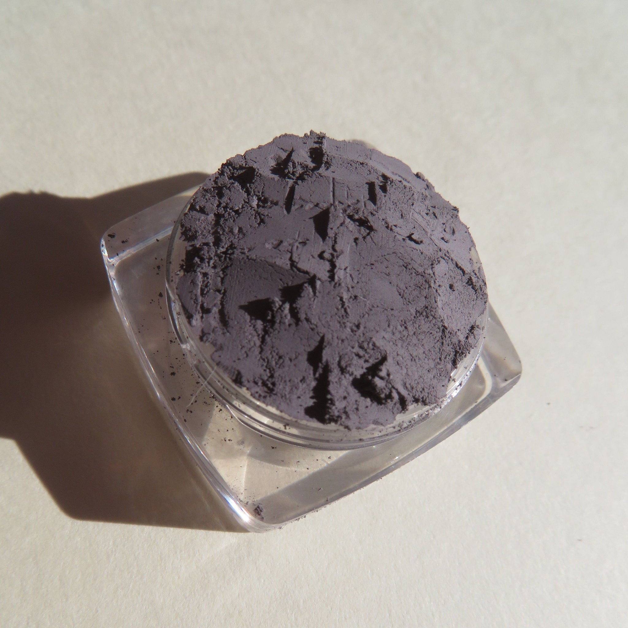 Powdered eyeshadow in gray, textured, in a clear plastic container