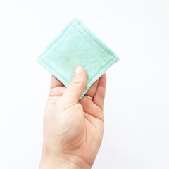 Reusable face pad, mint green square, soft material, held in hand