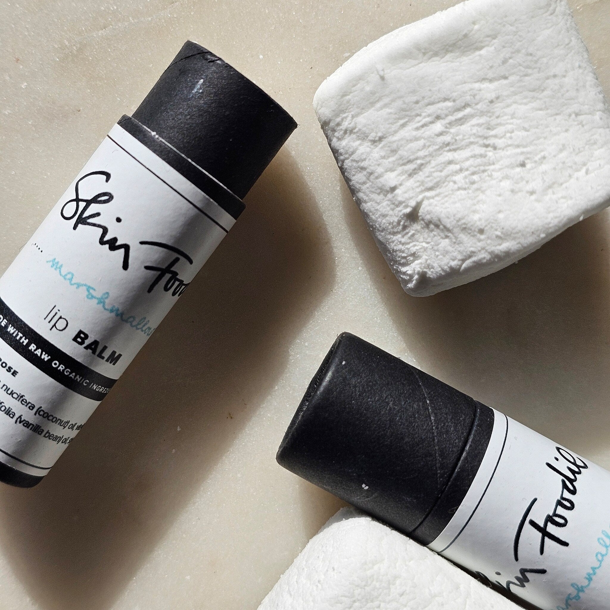 Lip balm with black tube and white label, "Skin Food" text, and white marshmallow pieces