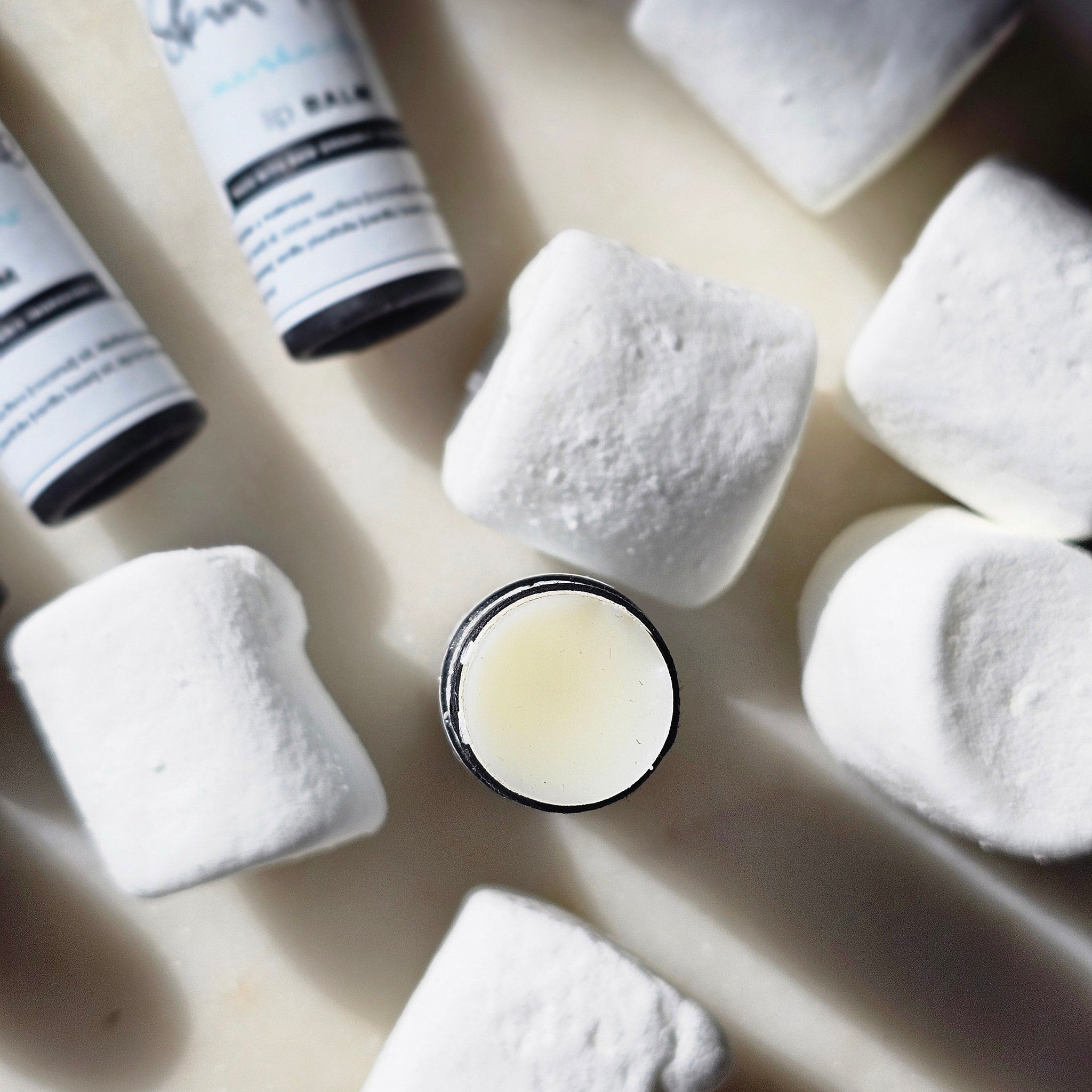 Lip balm with white and black packaging and white marshmallows on a light surface