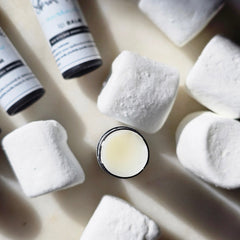 Lip balm with white and black packaging and white marshmallows on a light surface