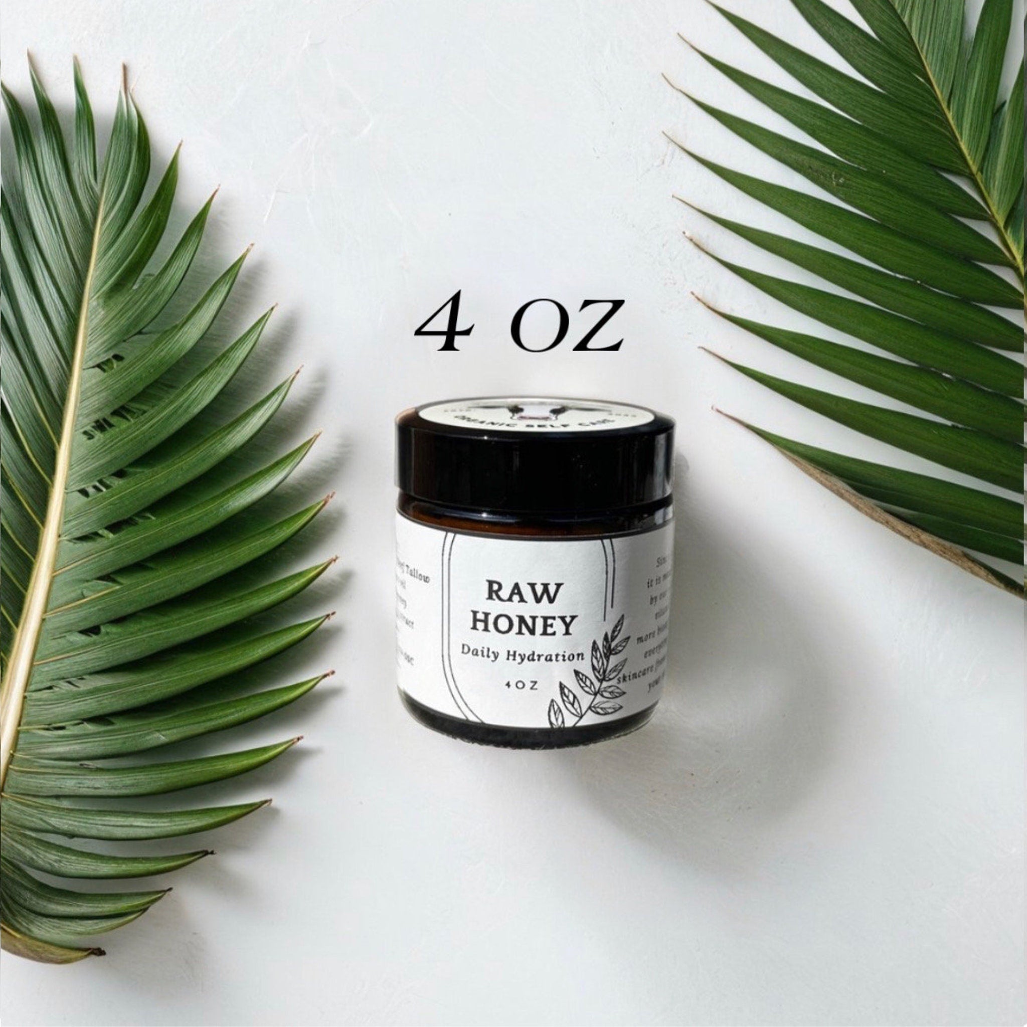Raw honey jar with black lid, white label, and green palm leaves on white background