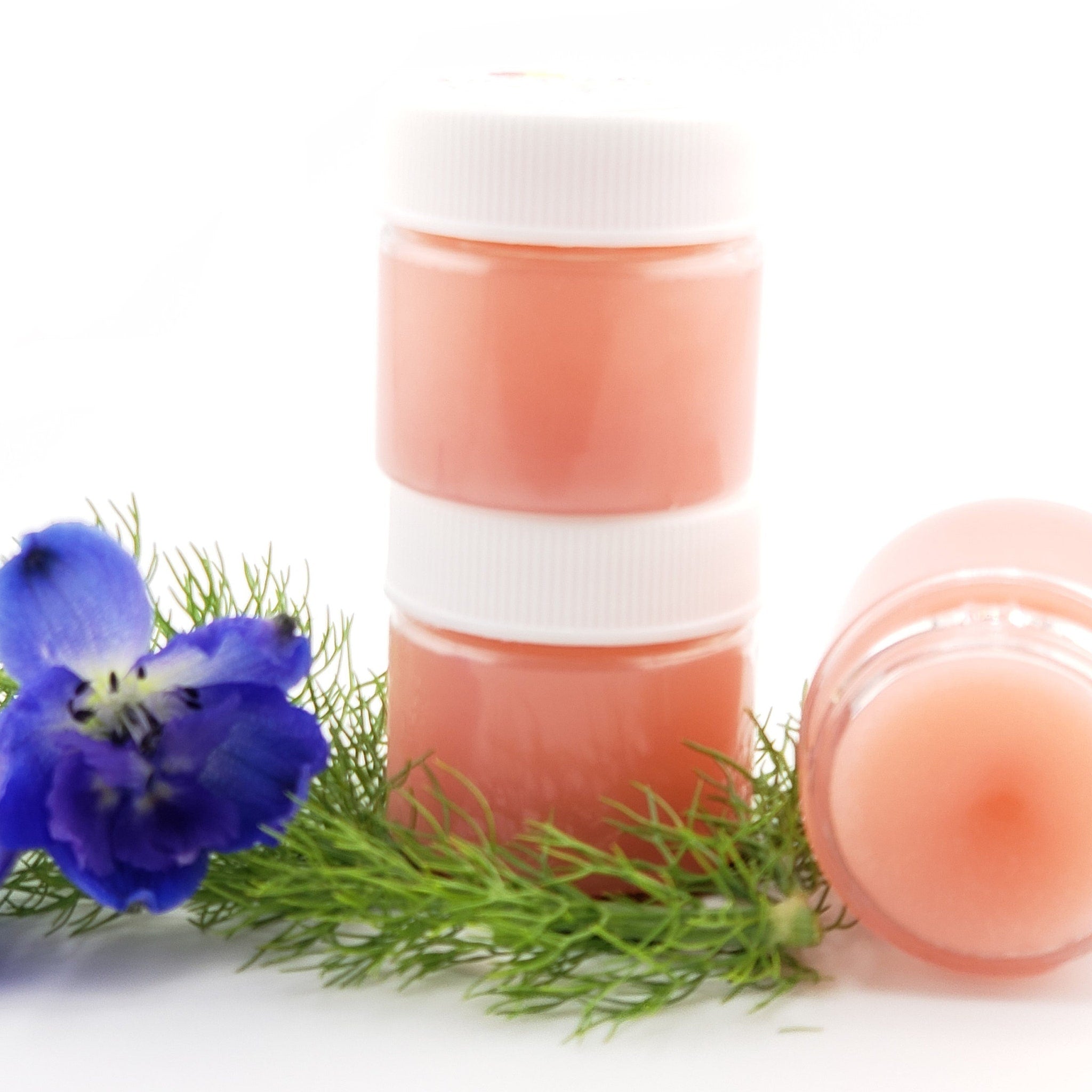 Pink jars with white lids, blue flower, and green sprigs on white background